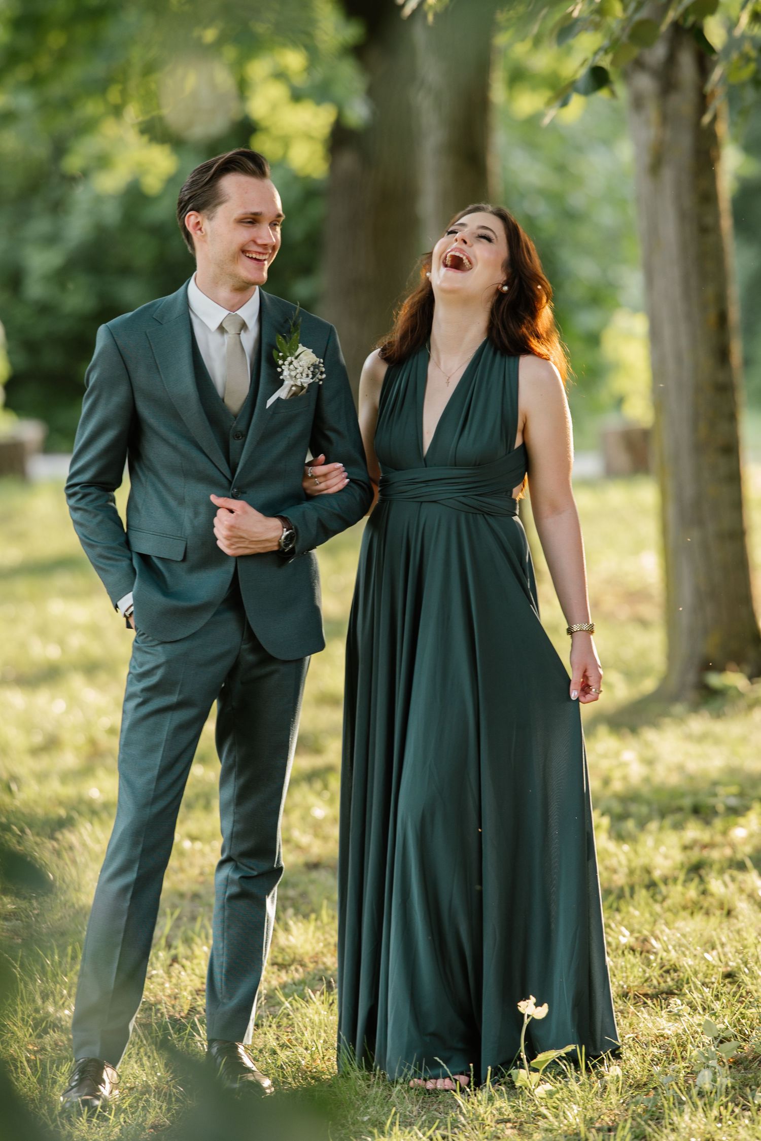 Couple sharing laughter during outdoor photo session among trees.