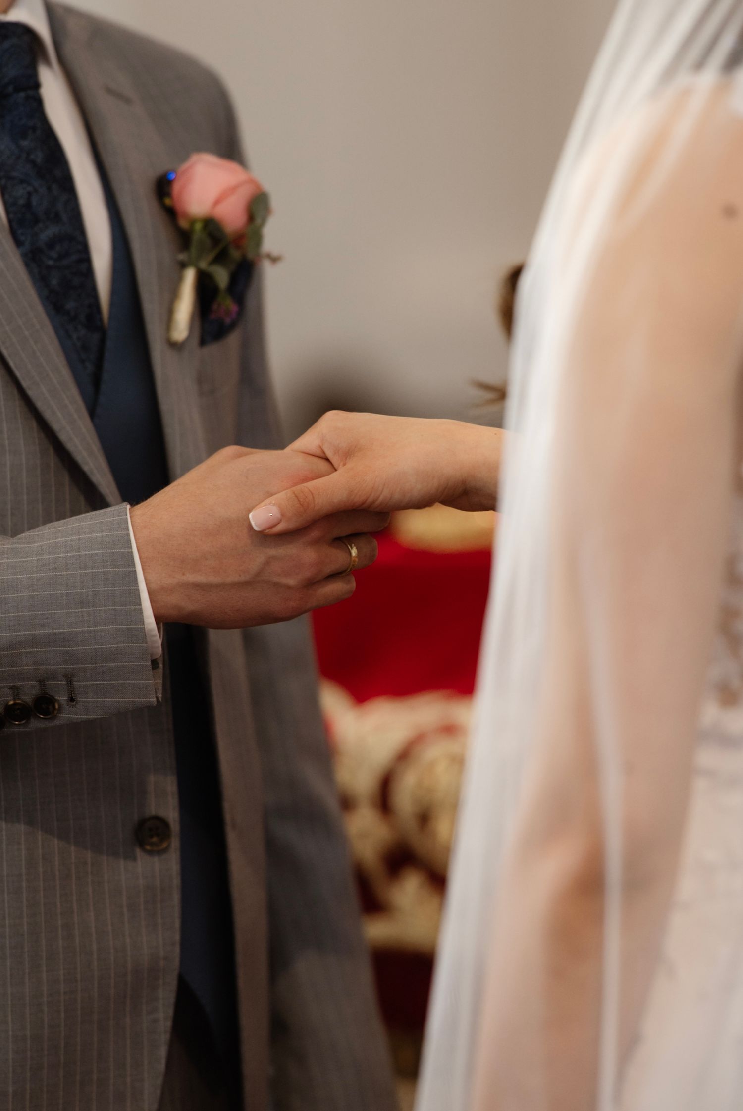 Bride and groom exchanging rings during wedding ceremony, groom in gray suit with pink boutonniere.