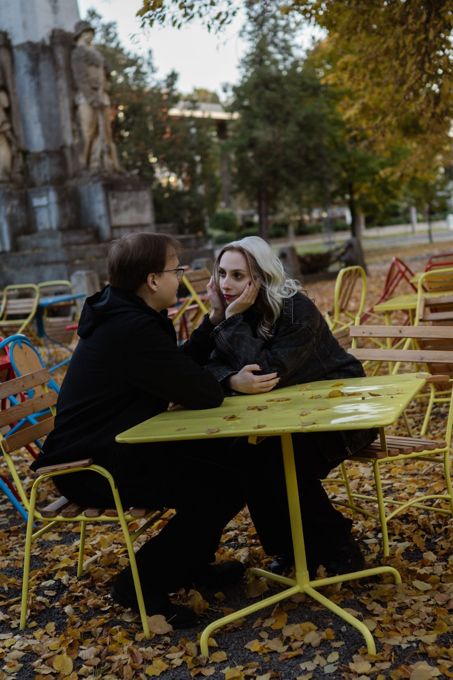 Couple shares intimate moment at outdoor table surrounded by autumn leaves.