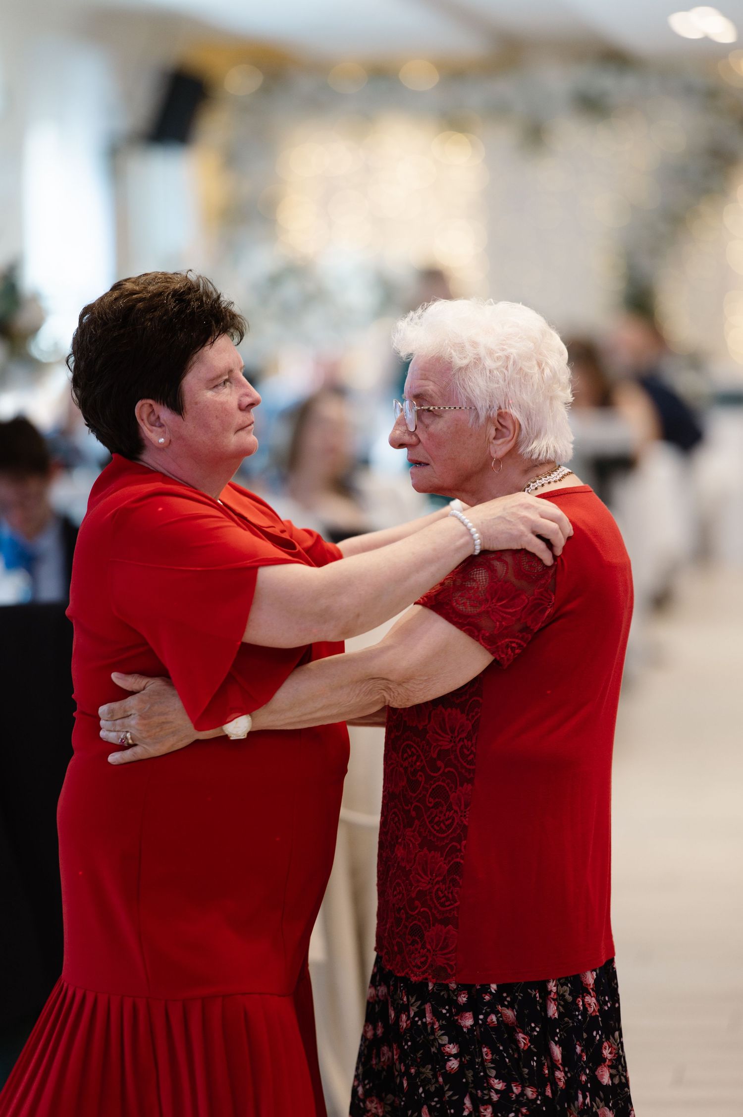 Two women in red dresses share an emotional embrace at a formal event.