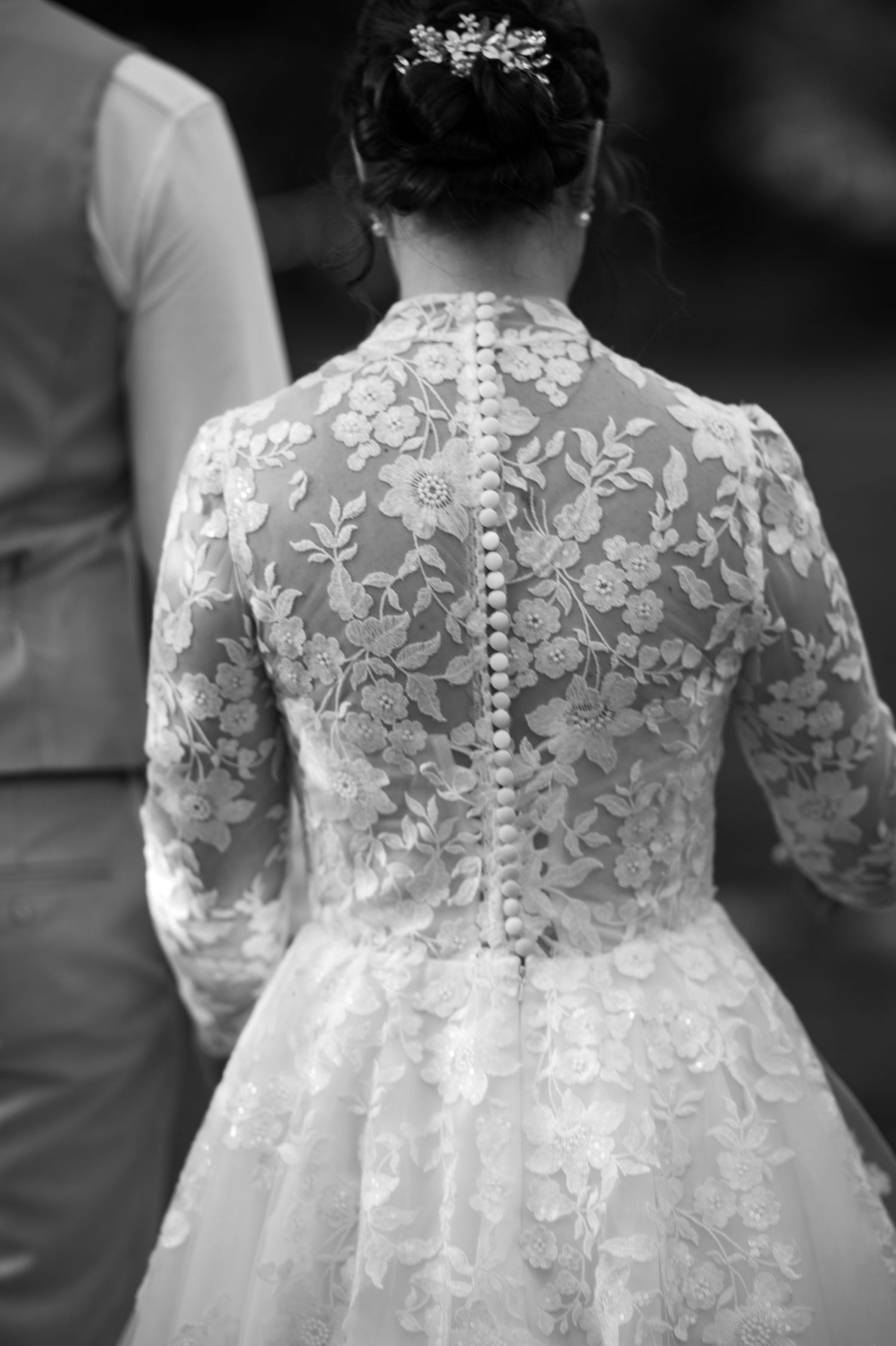 Detailed back of a wedding dress shows intricate lace patterns and button closures.