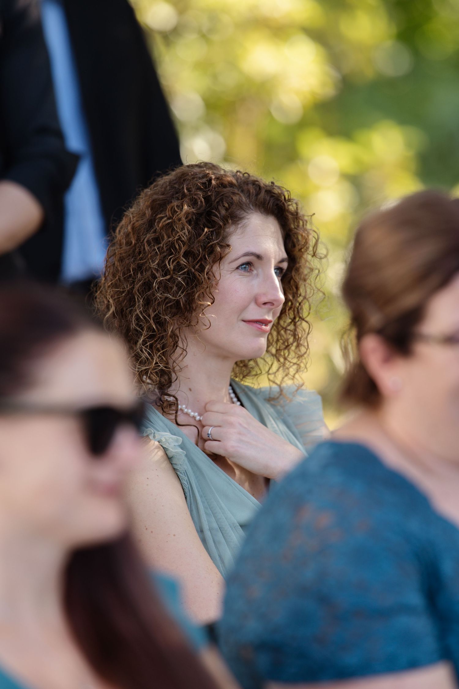 Wedding guest with curly hair watching ceremony outdoors.