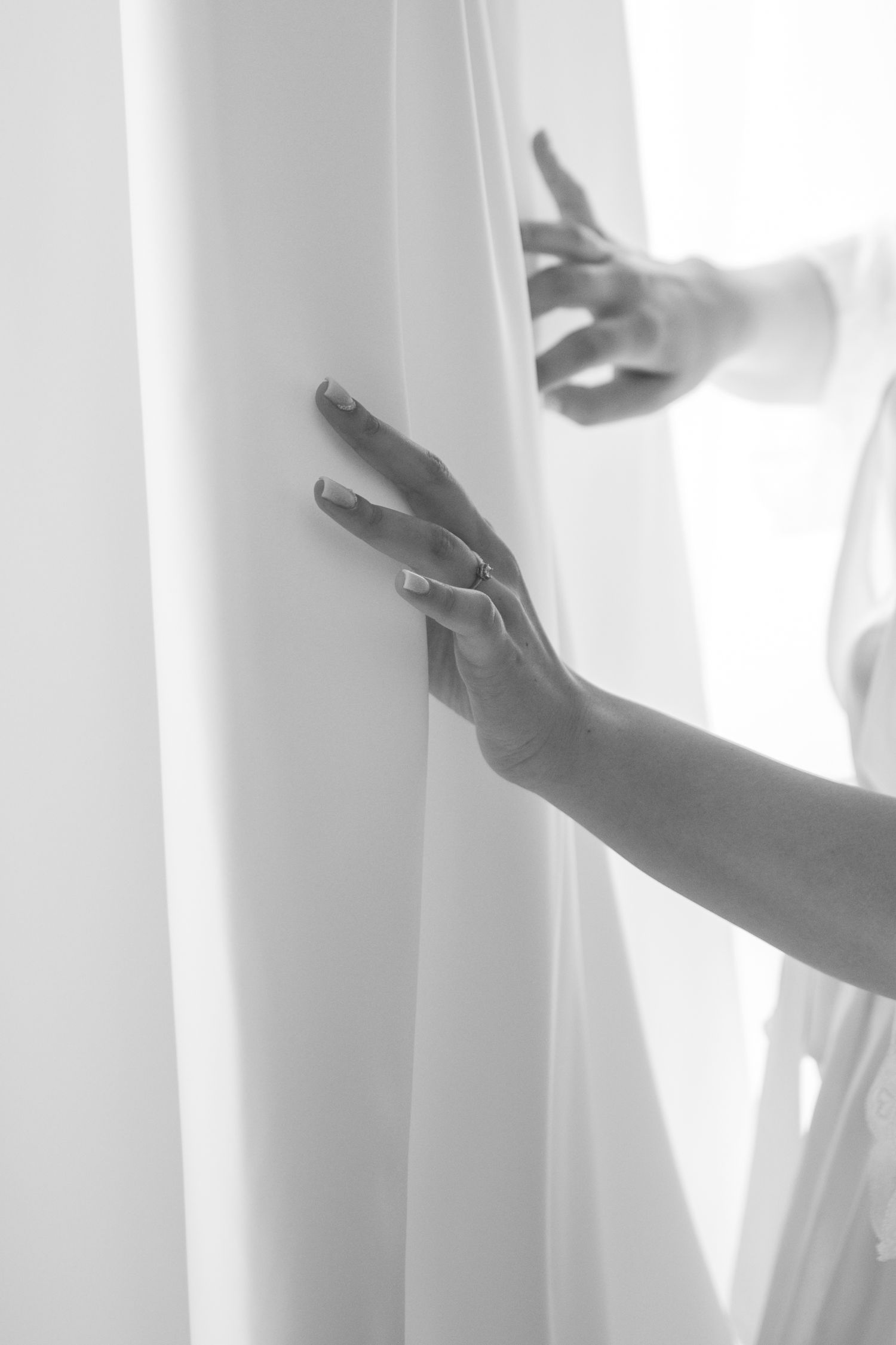 Artistic black and white image of hands against white flowing curtains.
