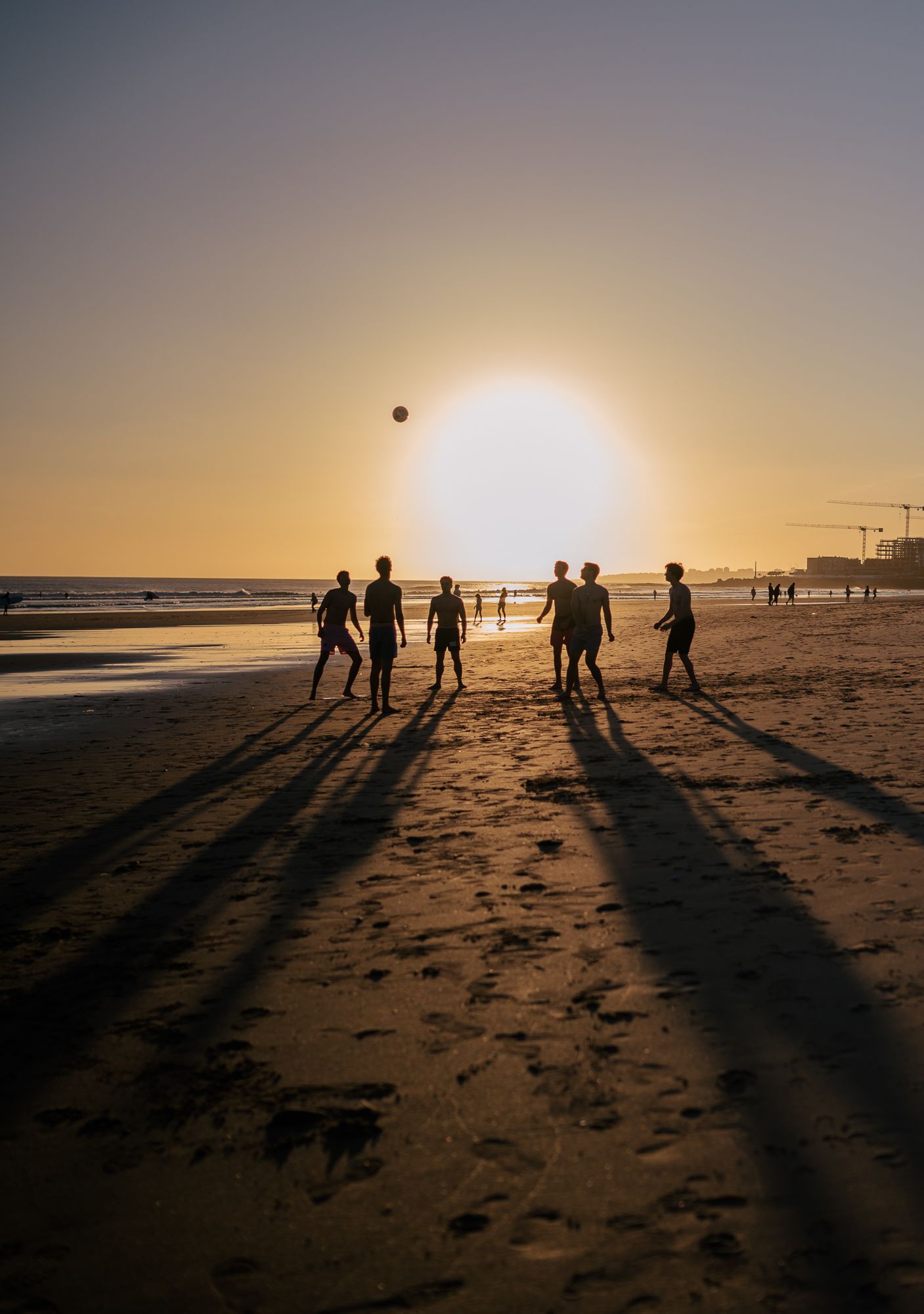 Silhouettes of people playing sports on a beach at sunset casting long shadows.