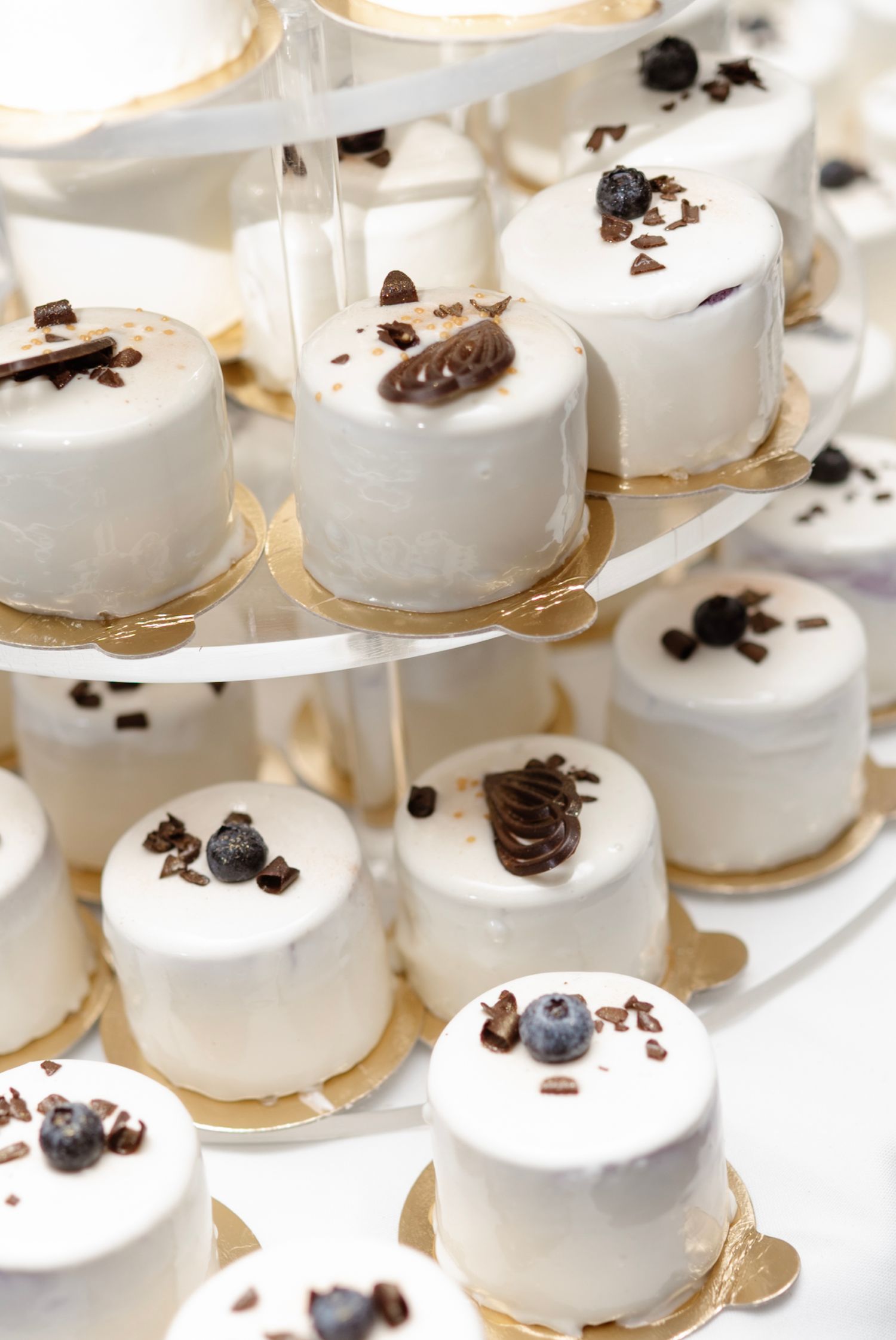 Elegant tiered display of white mousse mini cakes topped with chocolate and fresh blueberries.