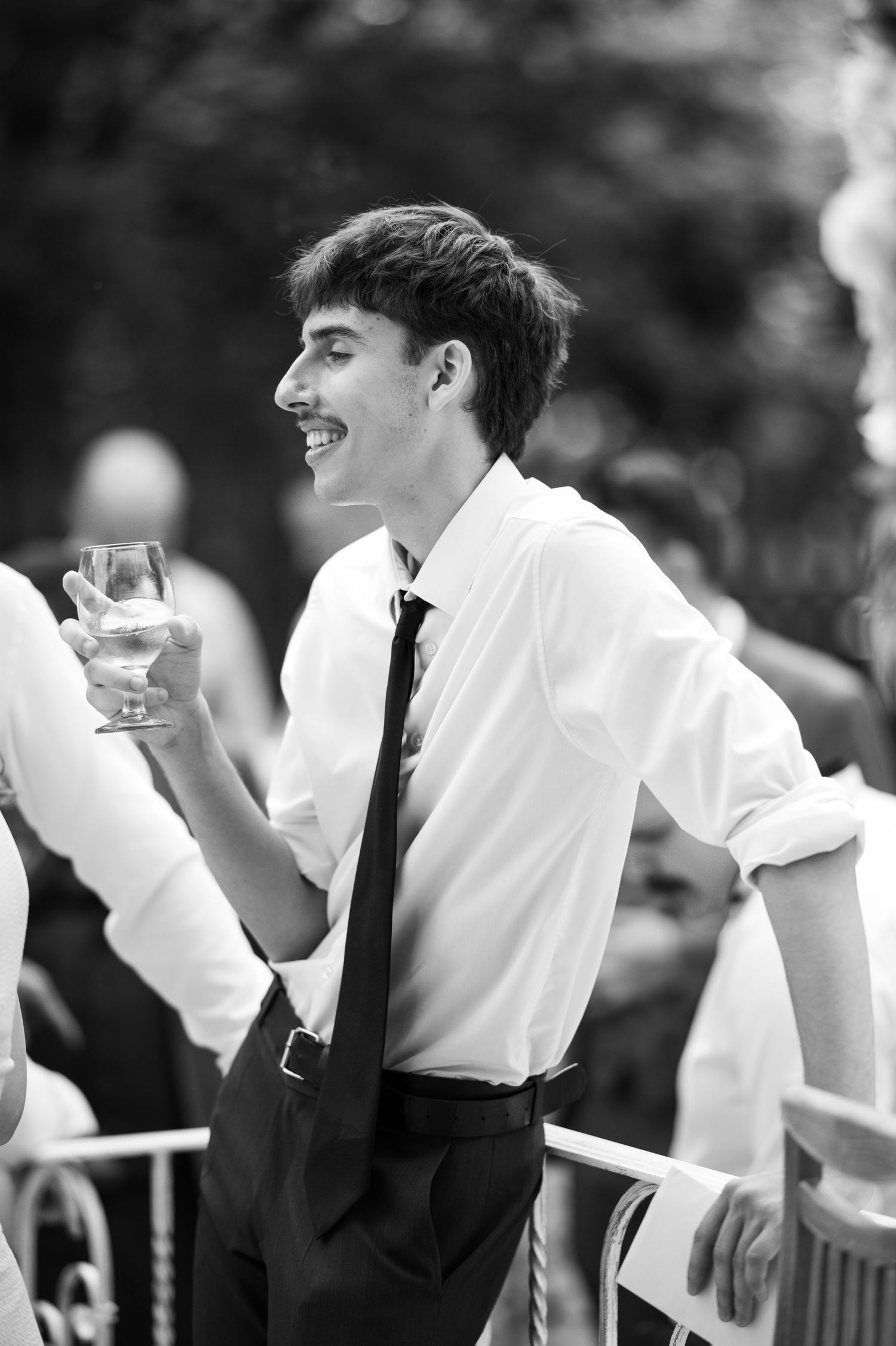 Wedding guests laugh and smile while enjoying drinks at an outdoor reception.