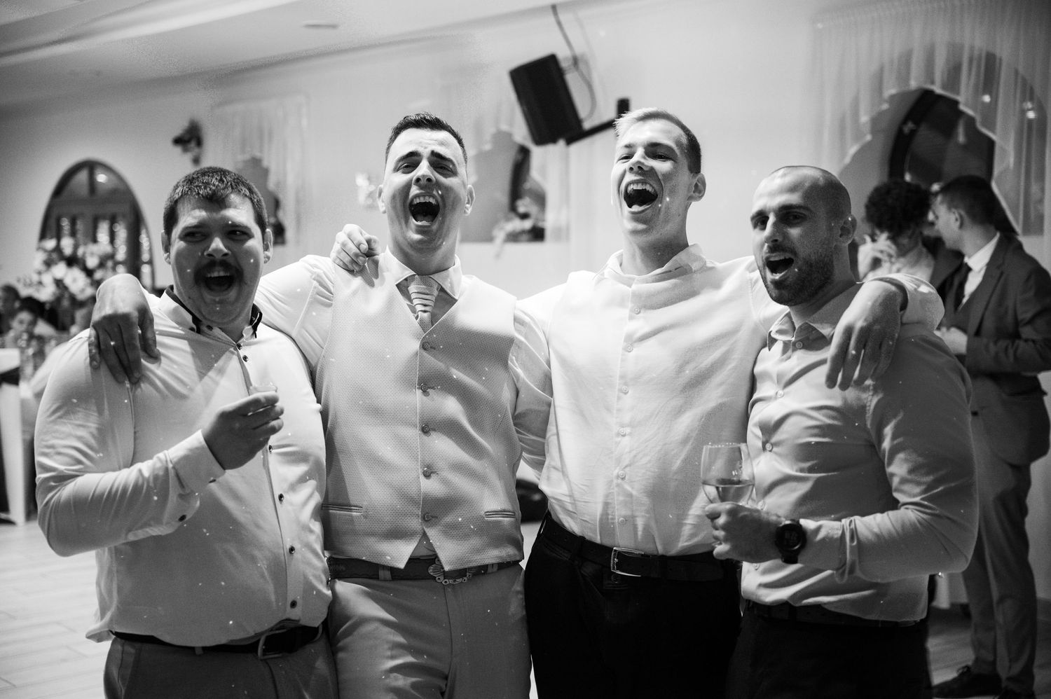 Groomsmen in white shirts celebrate energetically on the dance floor.