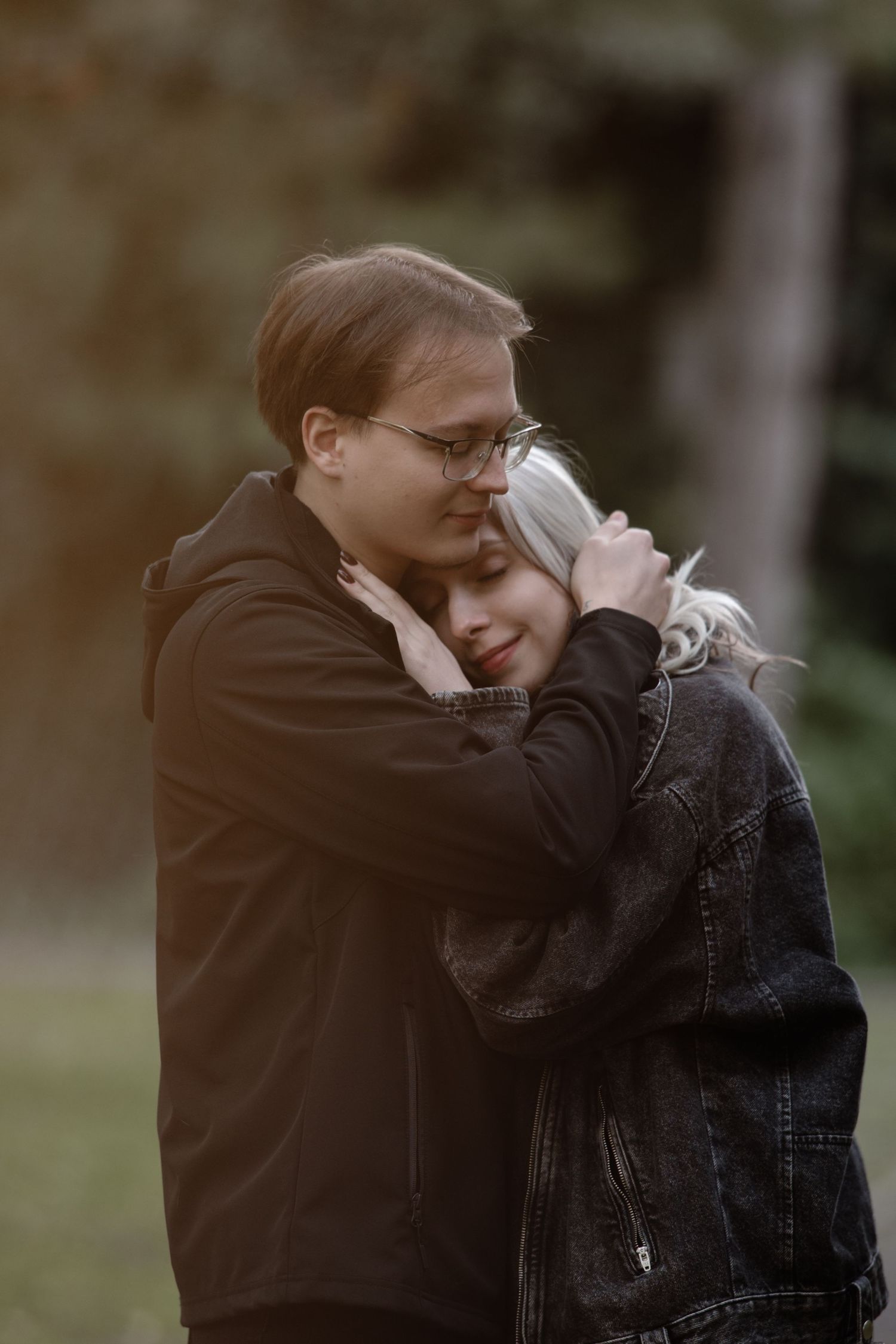 Couple sharing an intimate embrace outdoors wearing dark clothing.