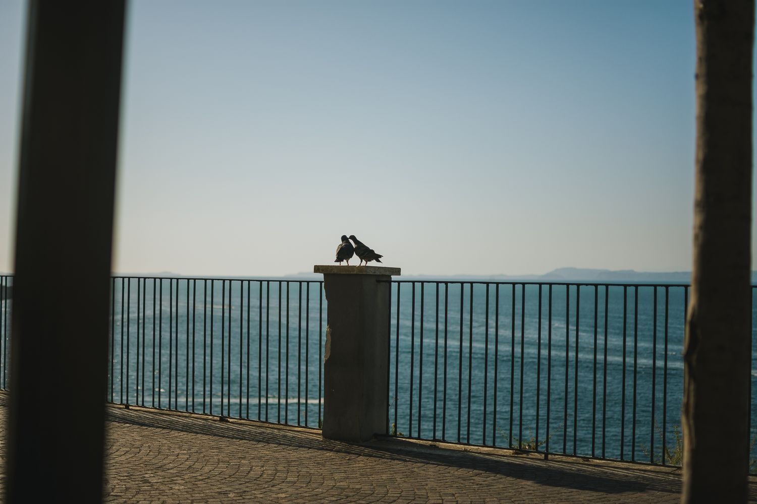 Scenic ocean view through metal railings with mountains in the distance.