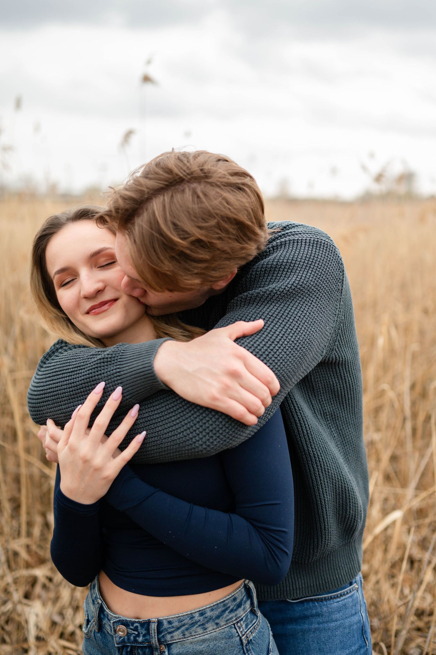 Intimate moments captured of a couple hugging in a field of tall grass during golden hour.
