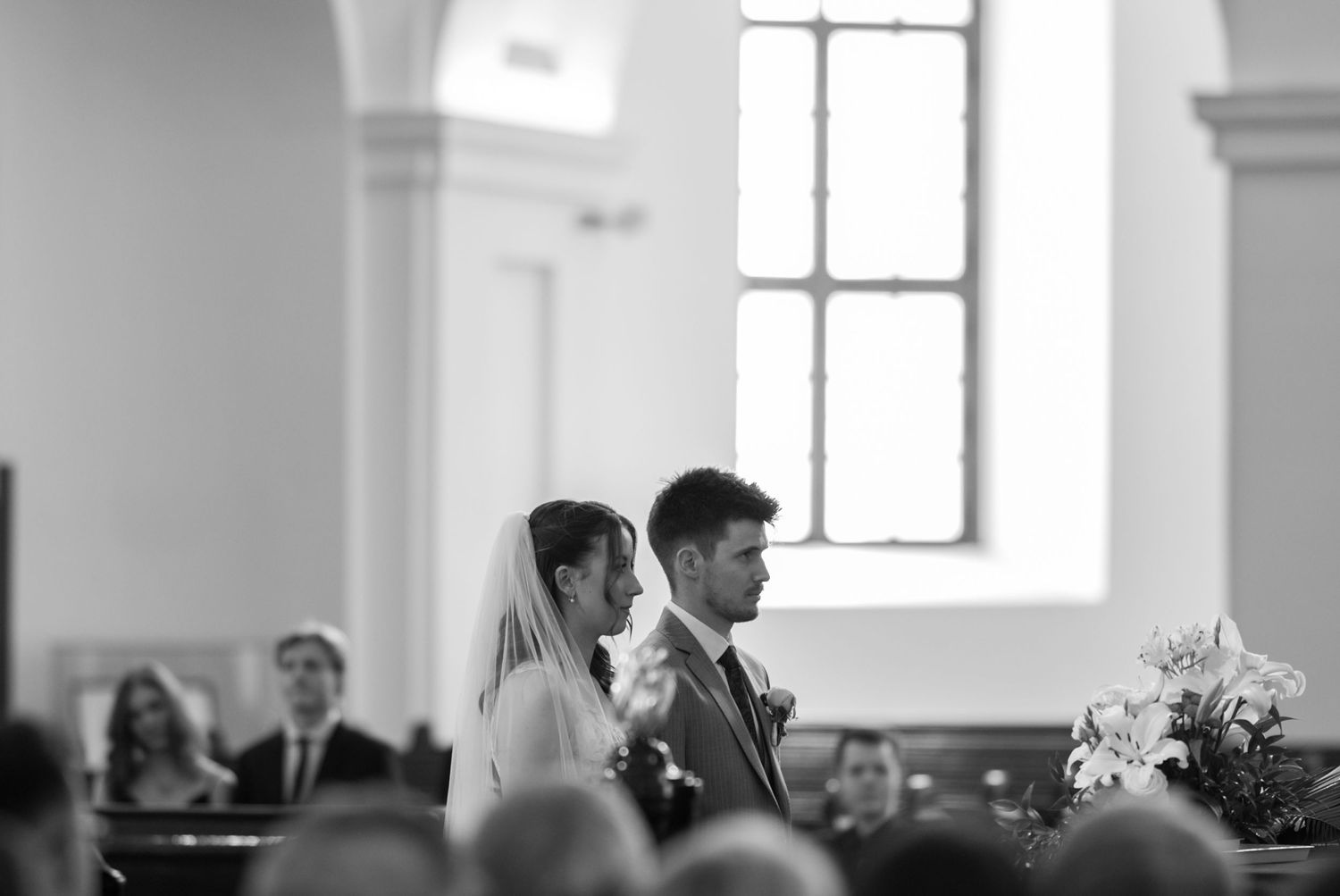 Black and white photo of a bride and groom standing at the altar during a church wedding ceremony.