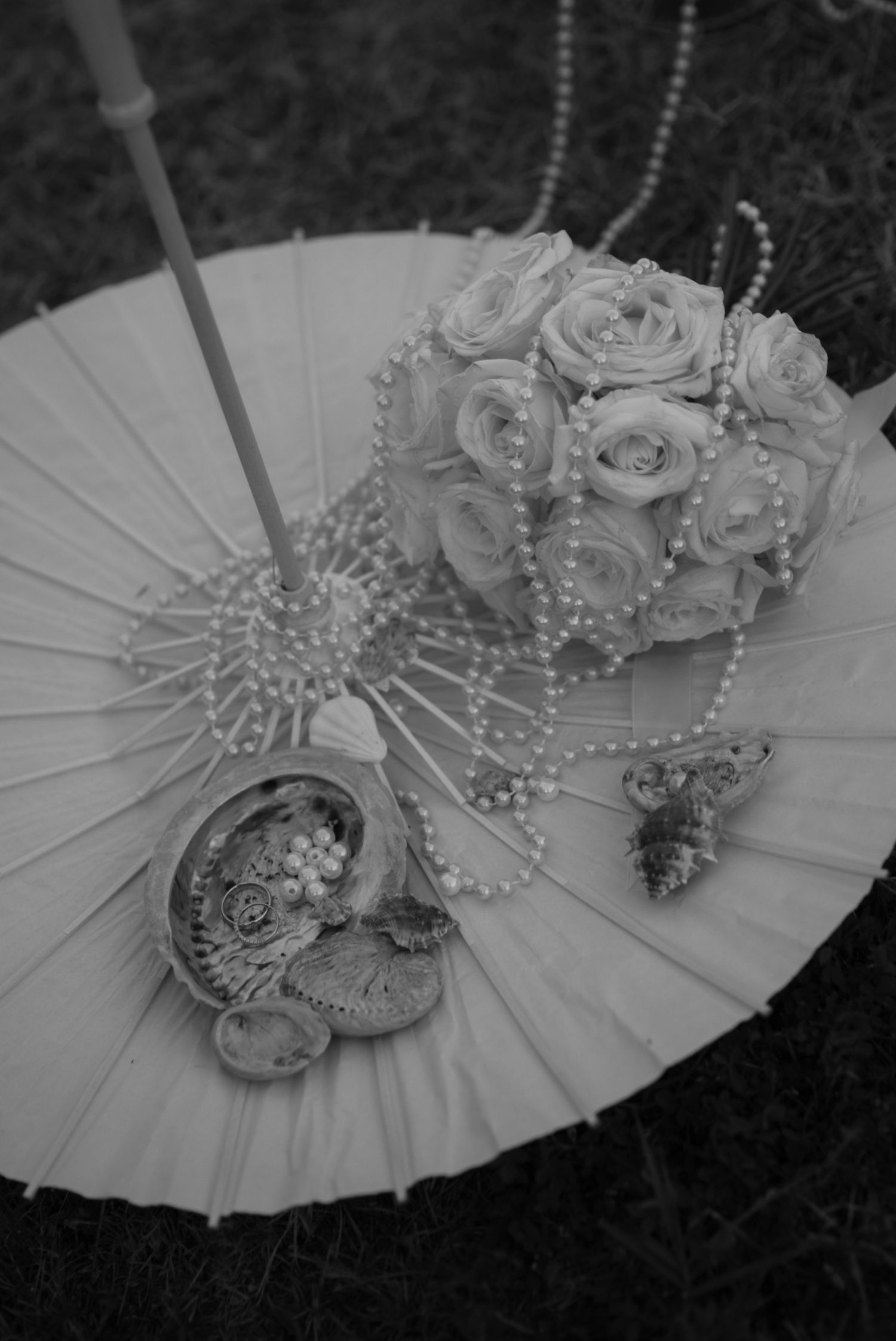 Black and white flat lay of bridal bouquet, pearls, and accessories on a white parasol.