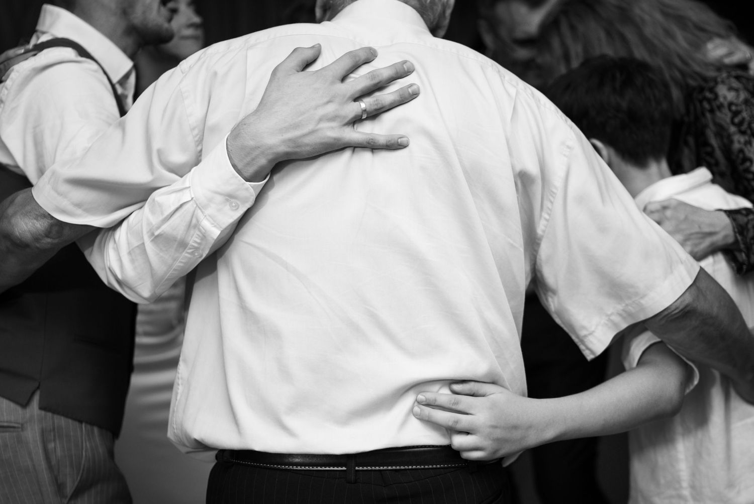 Black and white photo of wedding guests embracing during a group dance at a reception.