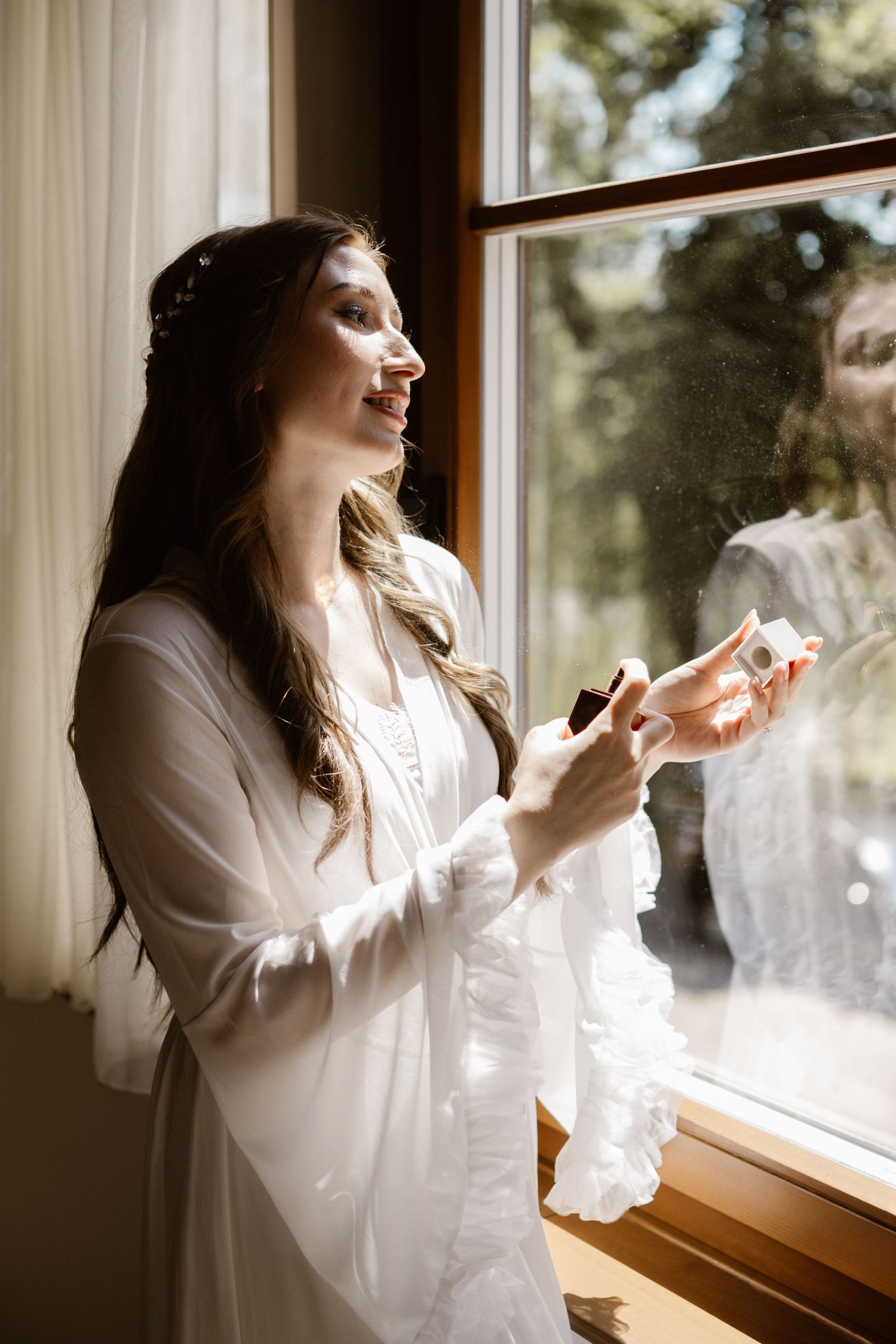 Person in white robe applying makeup by window in morning light.