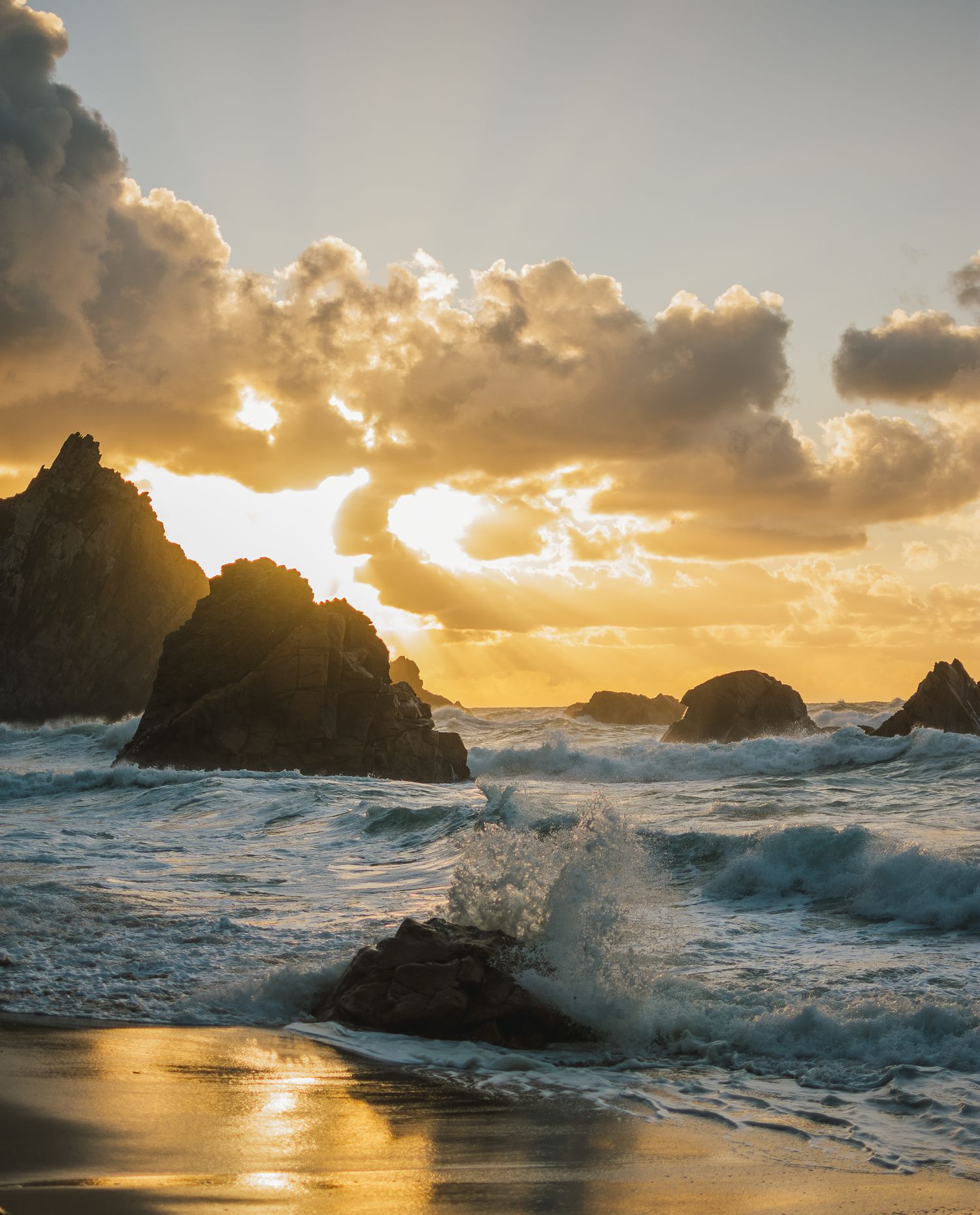 Dramatic waves crash against coastal rocks during a golden sunset over Big Sur's rugged coastline.