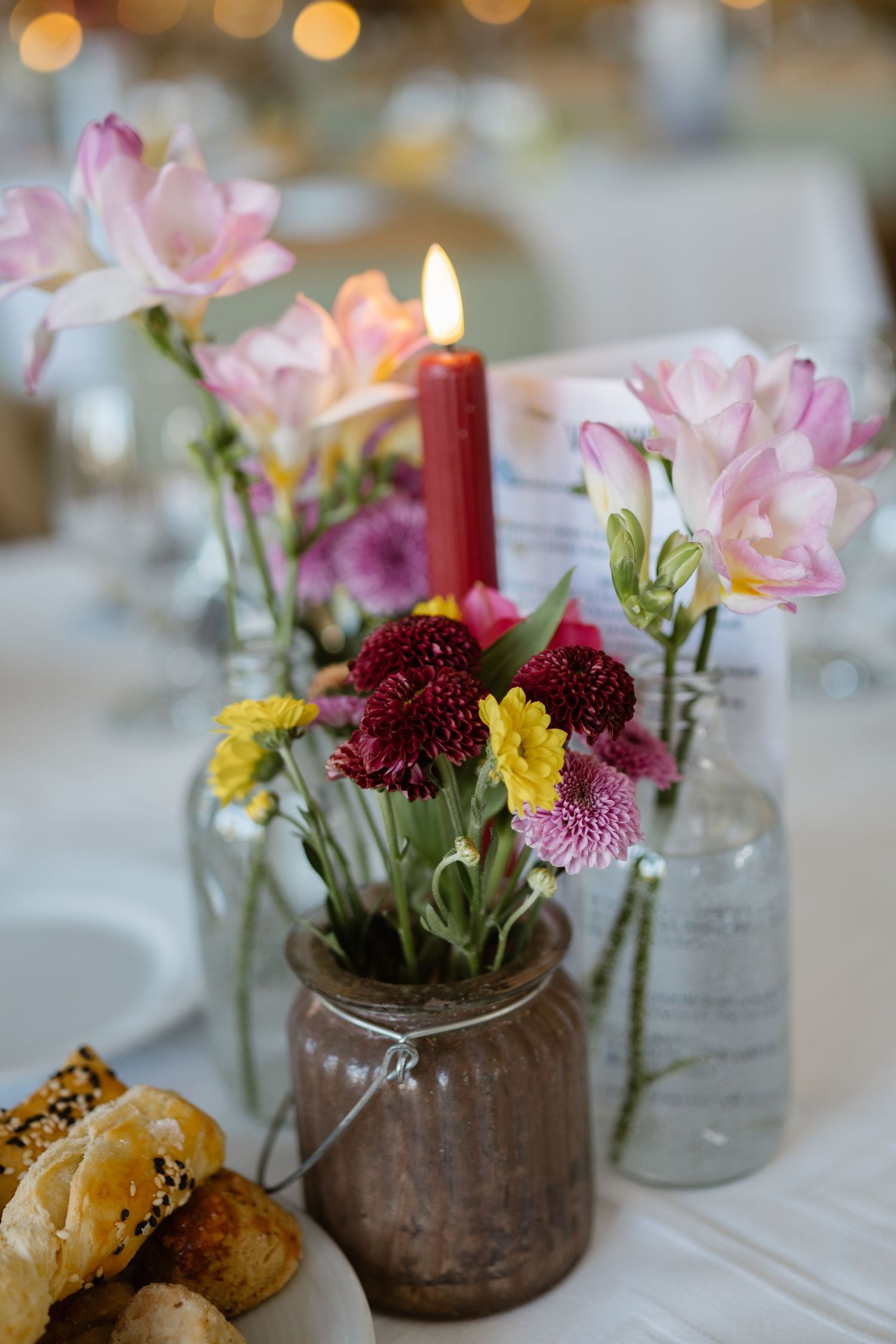 Rustic table centerpieces featuring pink flowers and burgundy dahlias in glass jars alongside fresh pastries.