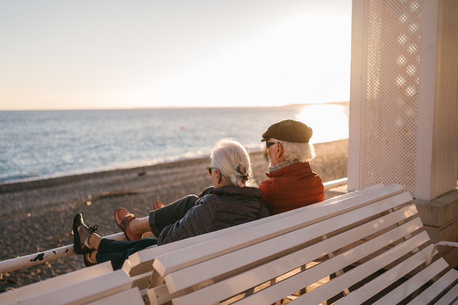 Two people relax on a wooden bench at sunset overlooking a scenic coastal view.