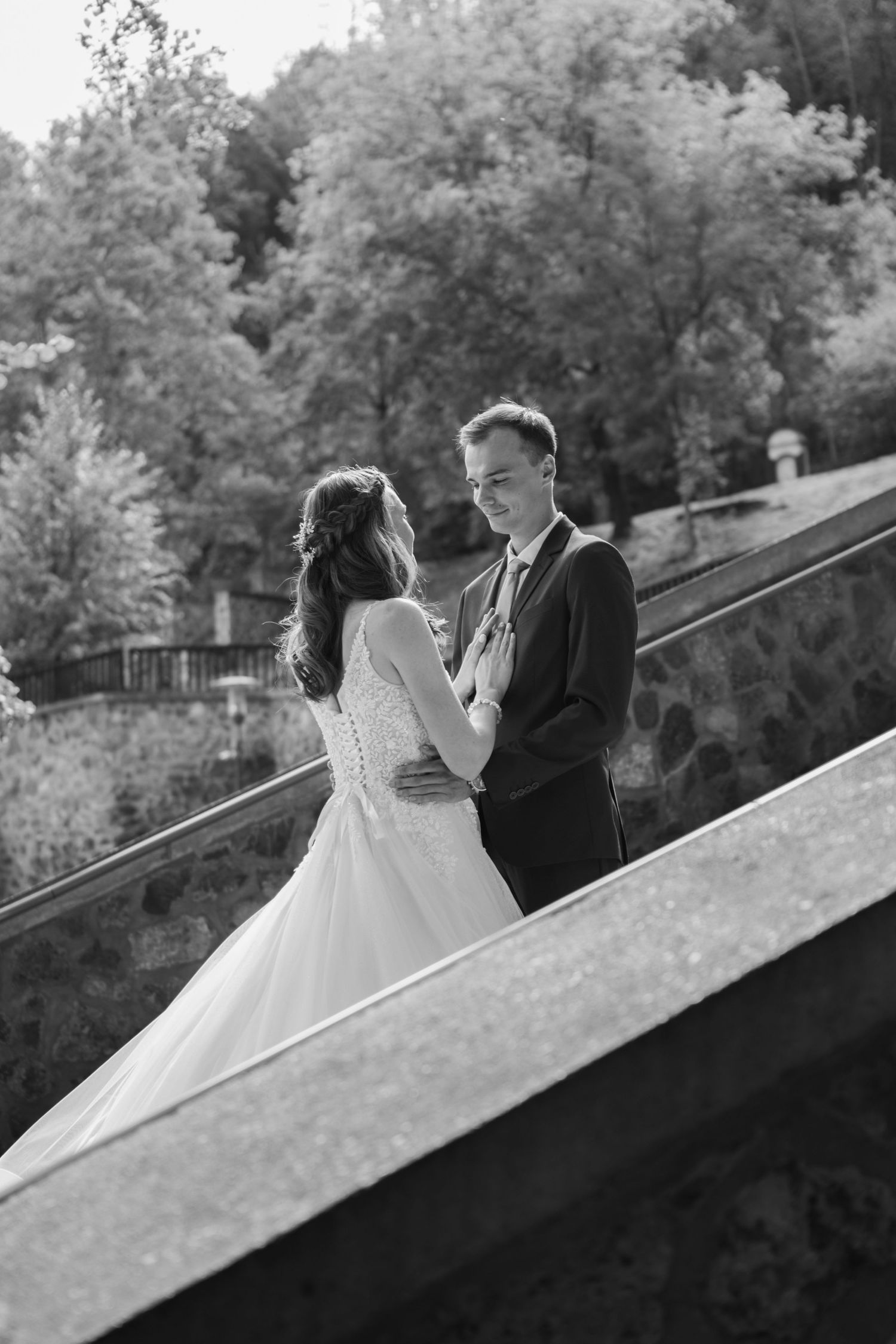 A romantic black and white photo of a couple on stone steps surrounded by trees.
