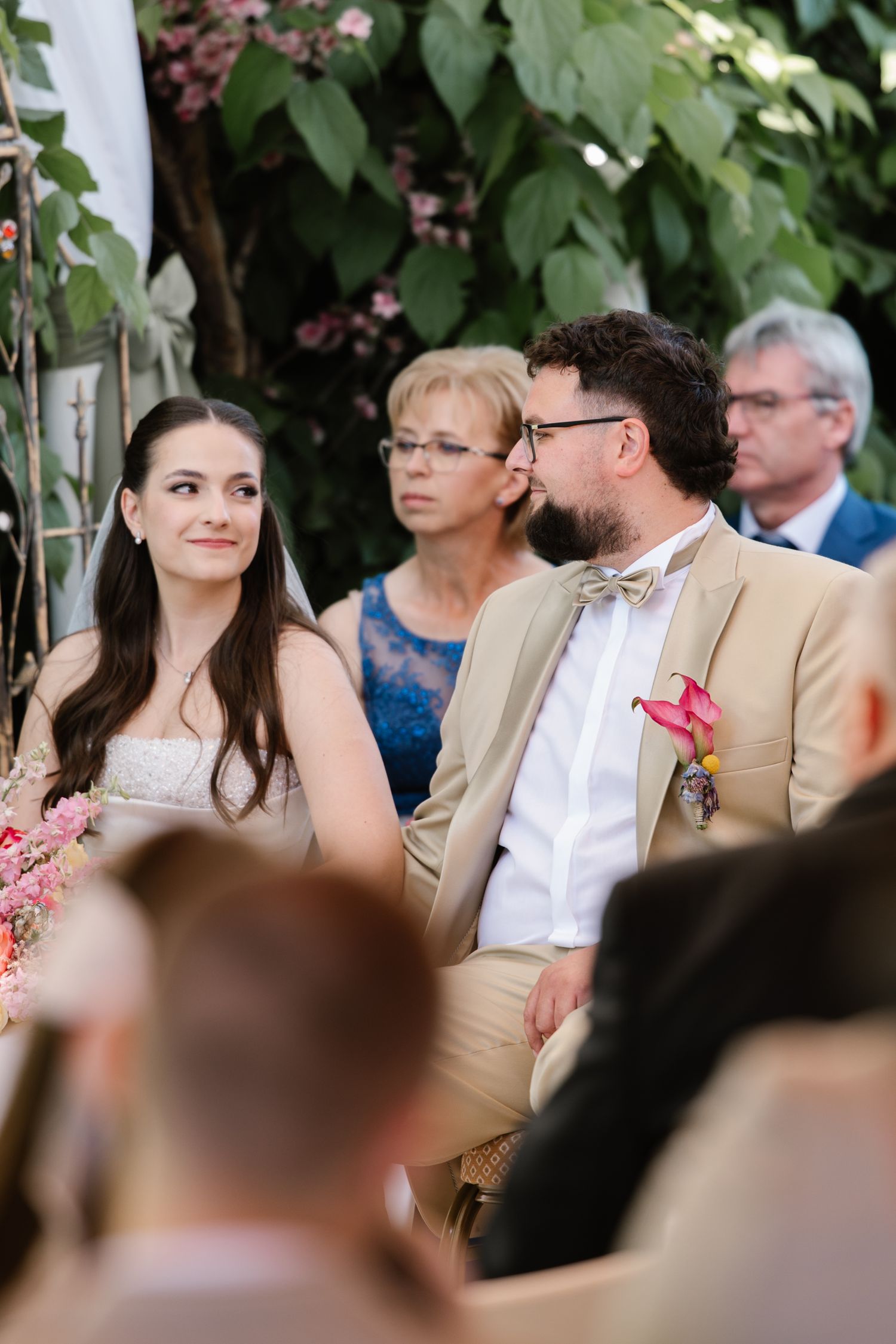 Young boy in formal attire sits with wedding guests during outdoor ceremony.