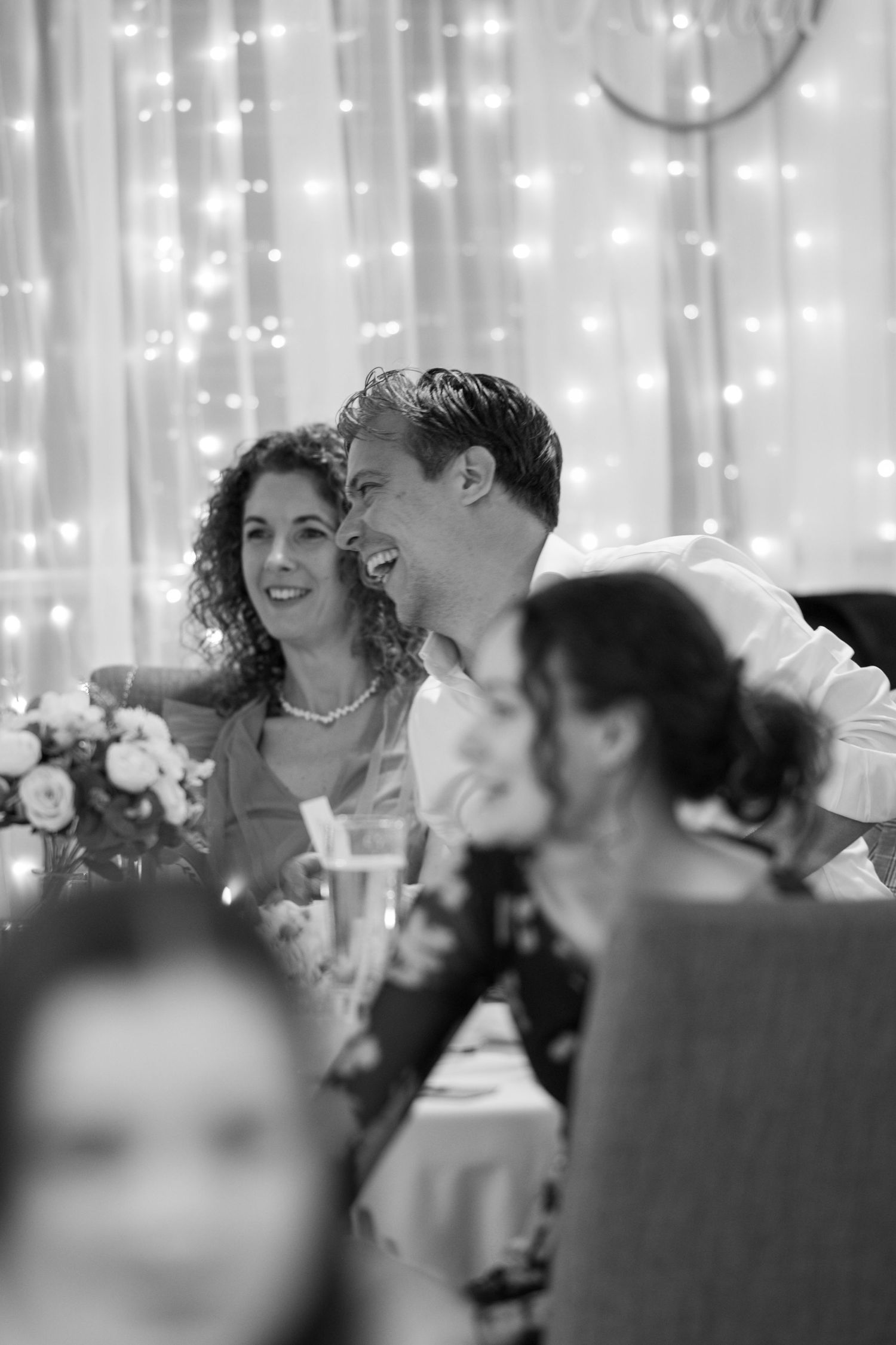 Wedding guests celebrate and laugh during reception under twinkling string lights.