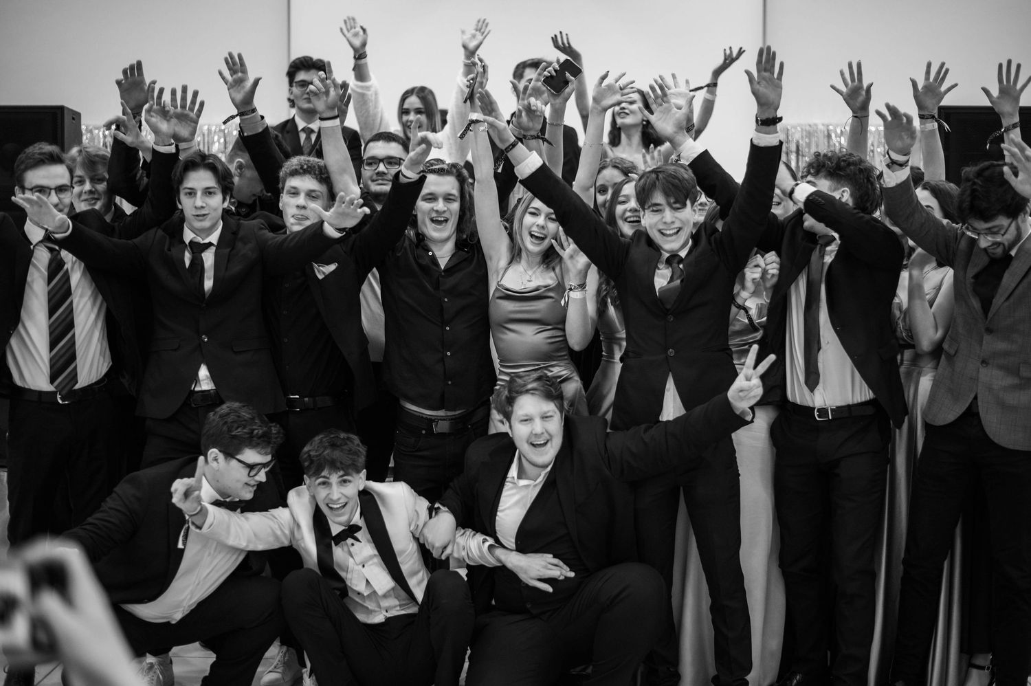 Large group of celebratory guests raising hands in unison at formal event.
