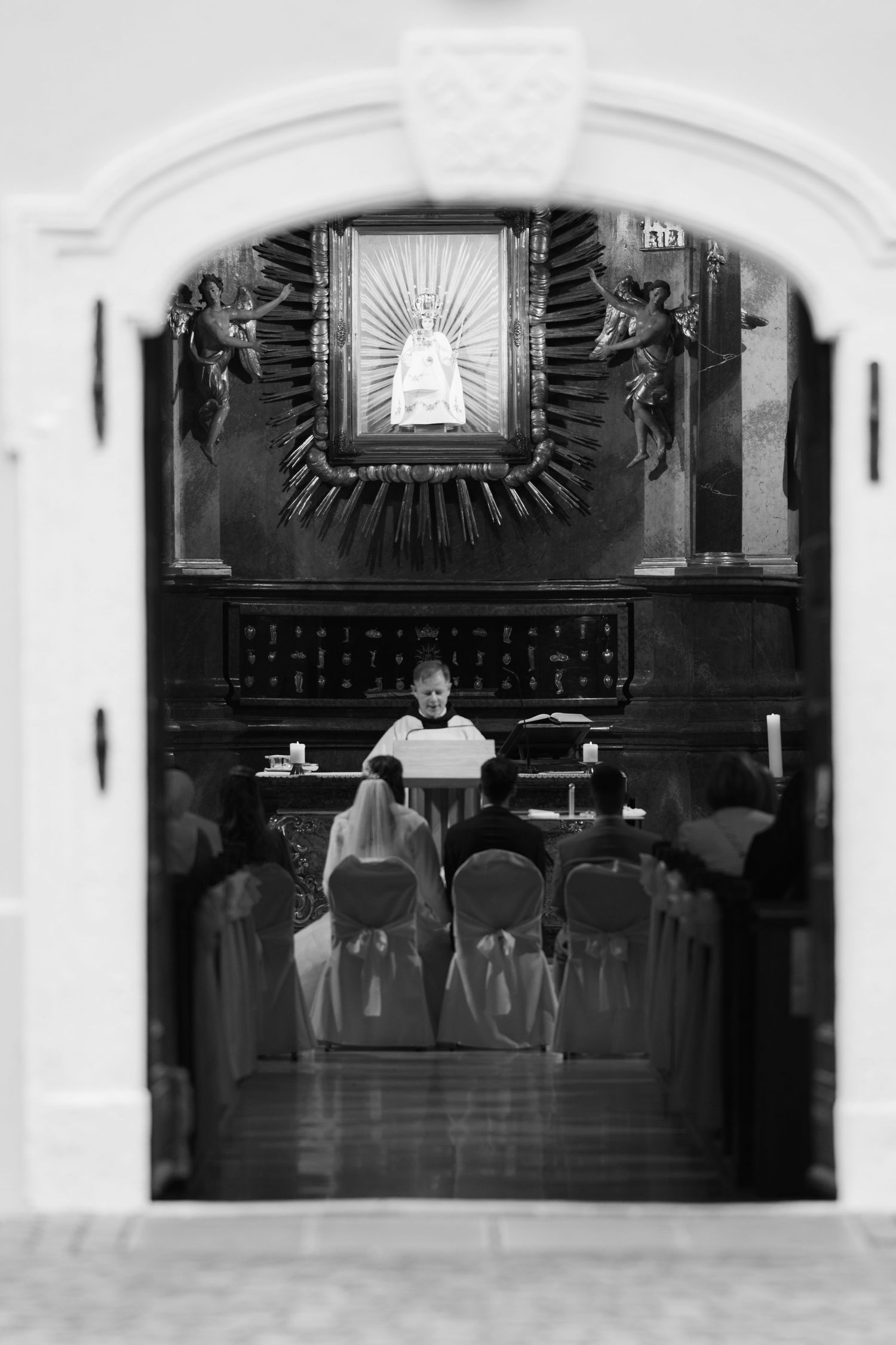 Black and white photo of a church interior with religious artwork and altar seen through an archway.