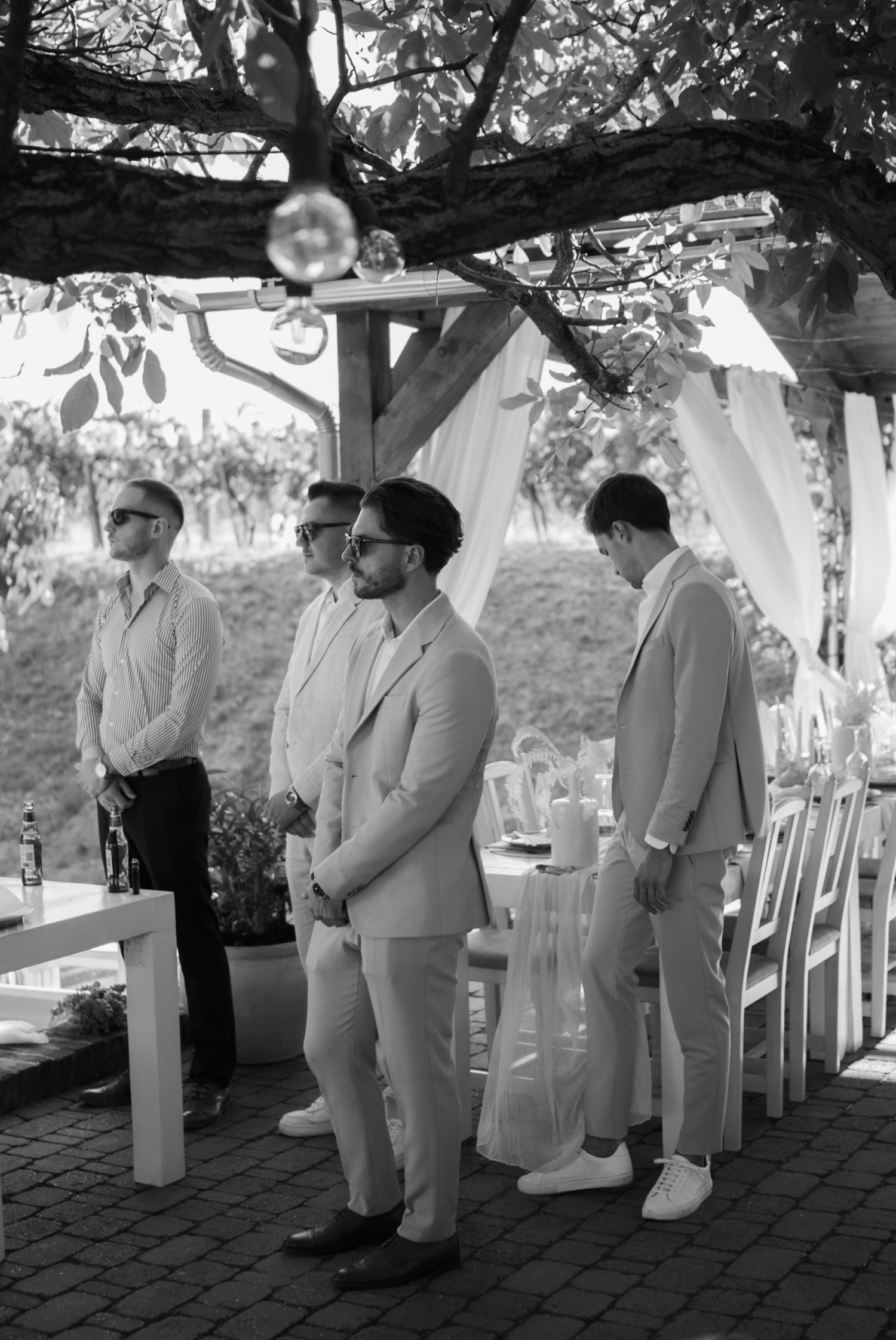 Groomsmen in light suits standing at outdoor wedding ceremony in black and white photo.