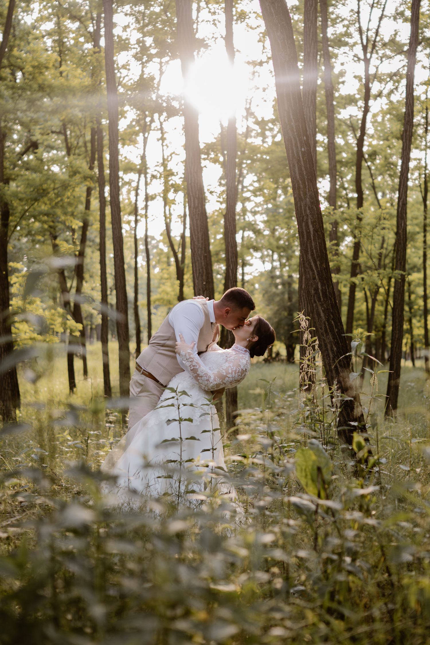 Romantic wedding portraits in a sunlit forest with wildflowers in the foreground.