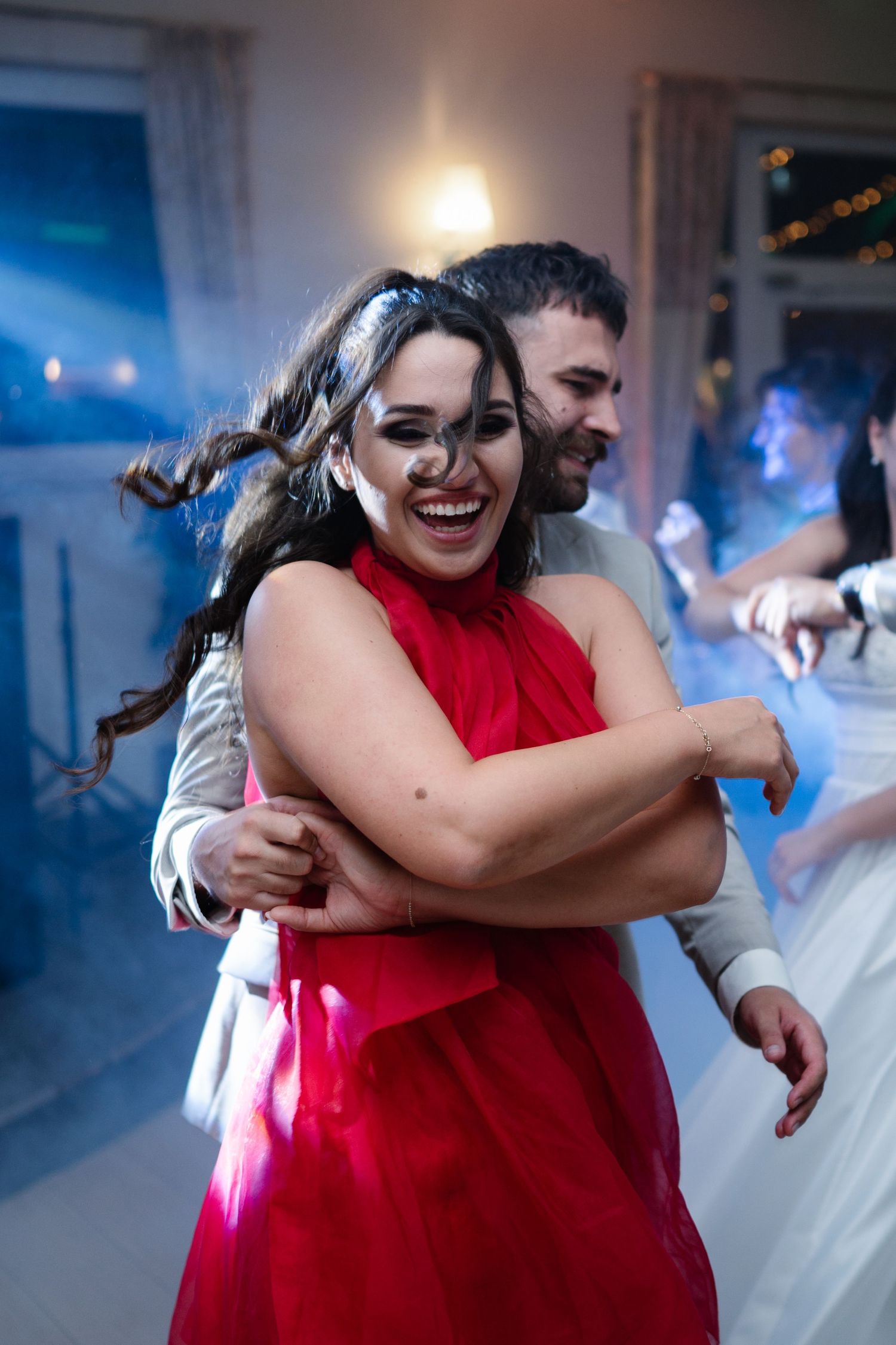 Wedding guests embrace while dancing during reception with blue atmospheric lighting.