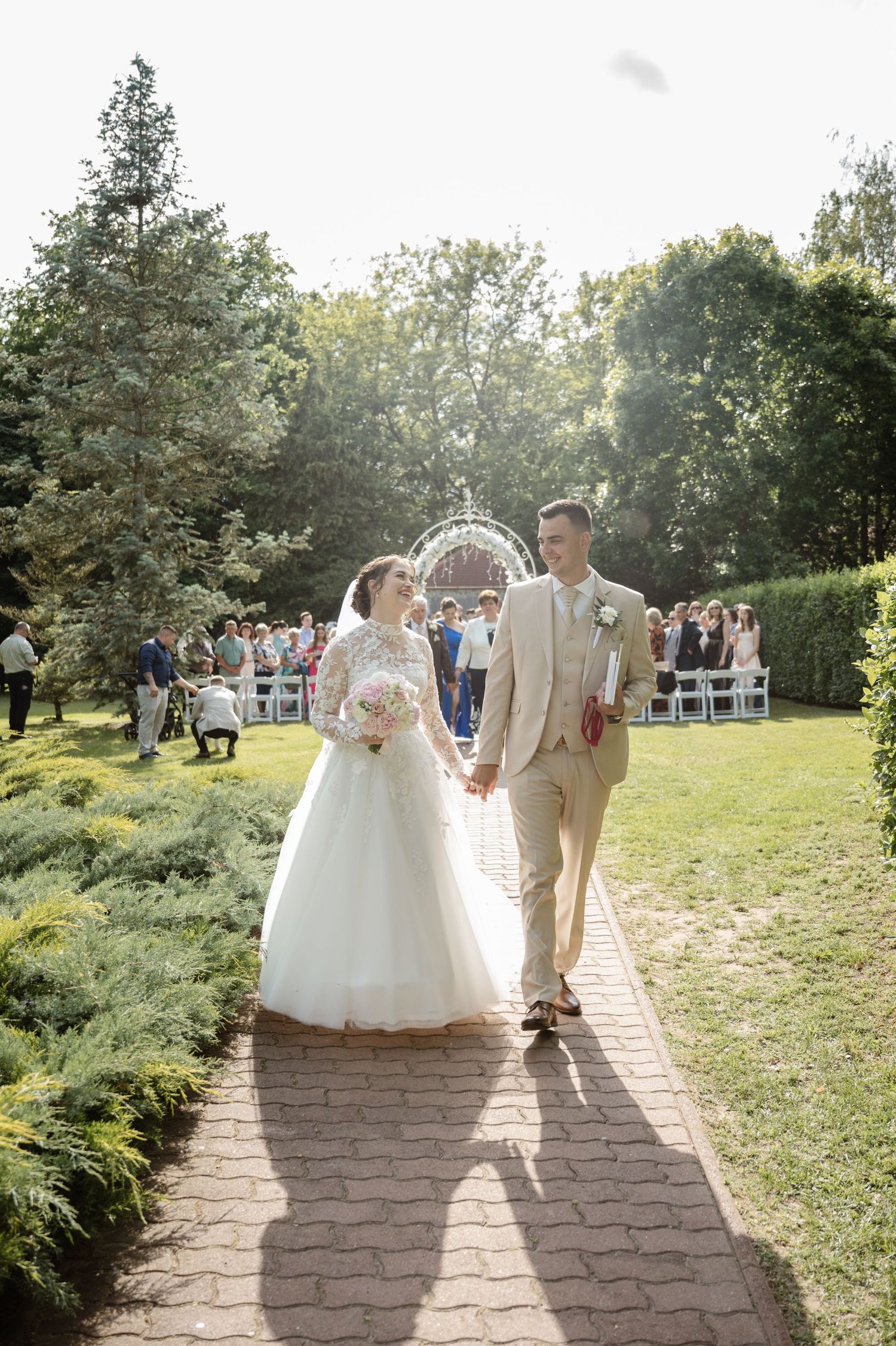 Newlyweds walking down a brick path after their outdoor ceremony as guests look on.