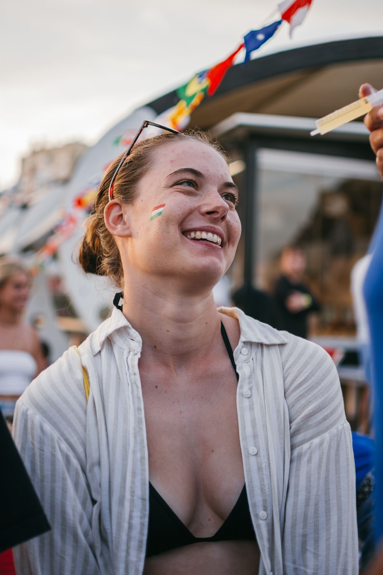 Person in white button-down shirt smiling at outdoor gathering with flags.