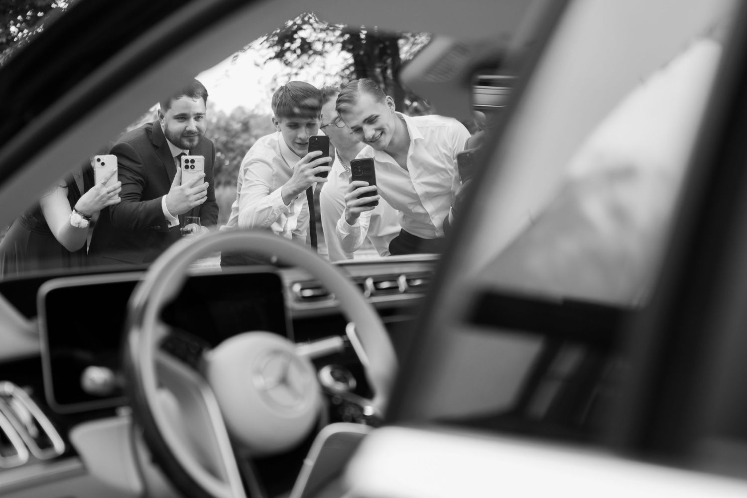 Black and white photo of wedding guests taking pictures through a car window.