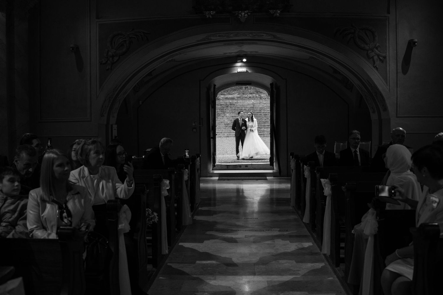 Dramatic black and white photo of a wedding ceremony in a church with silhouetted guests in pews.
