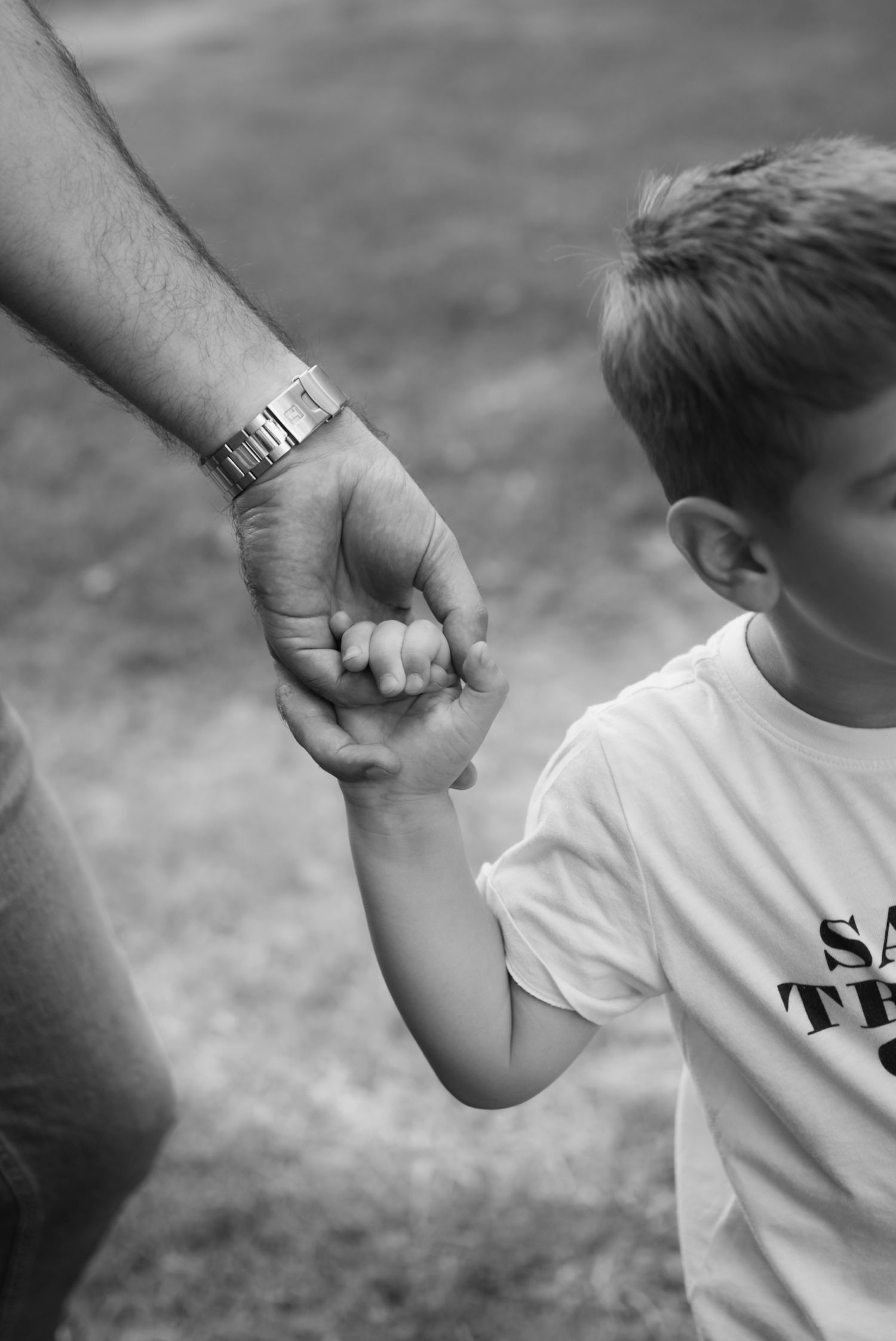 Black and white photo of a child holding an adult's hand outdoors, symbolizing trust and family bond.