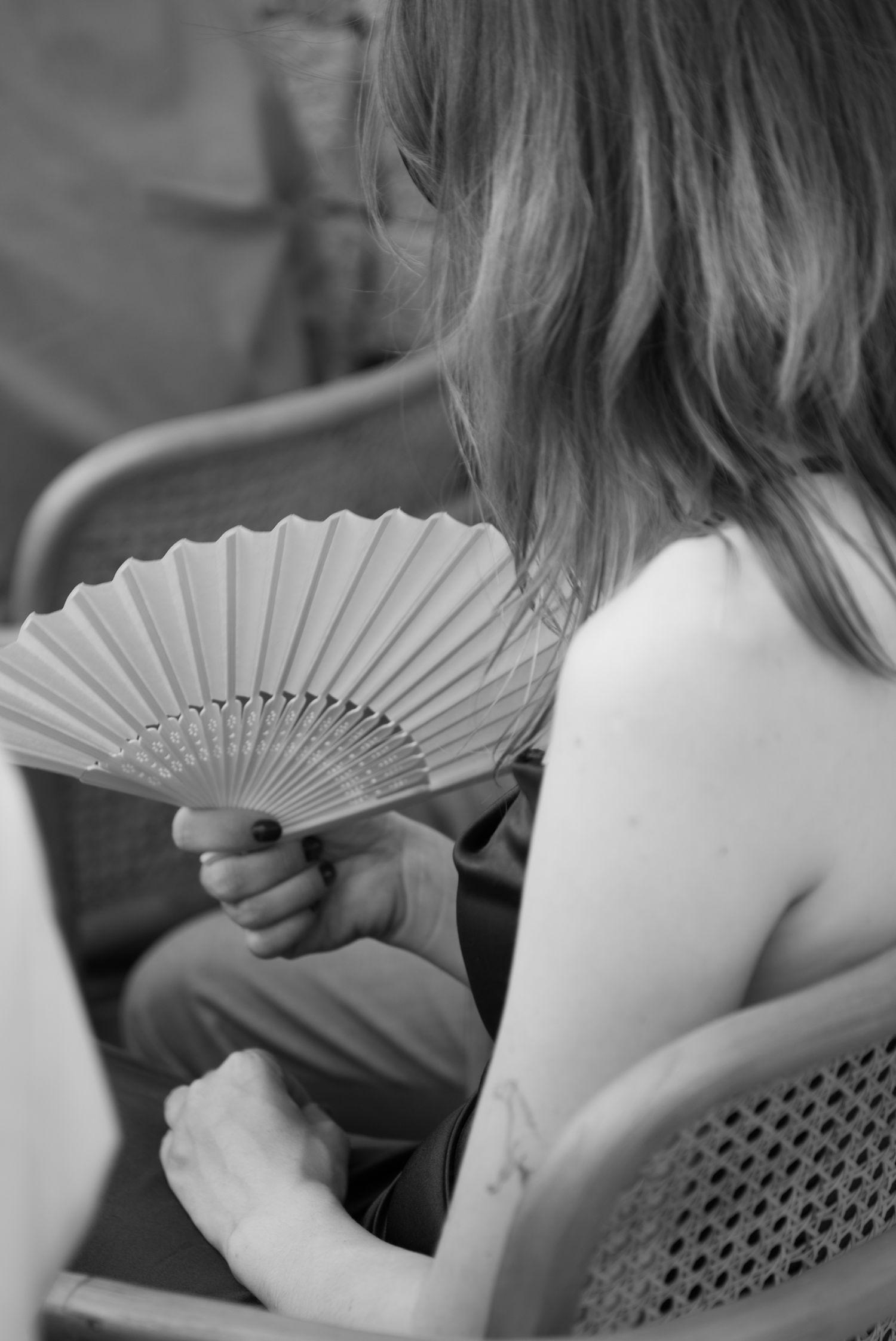 Black and white photo of a woman holding a pleated hand fan at an outdoor event.