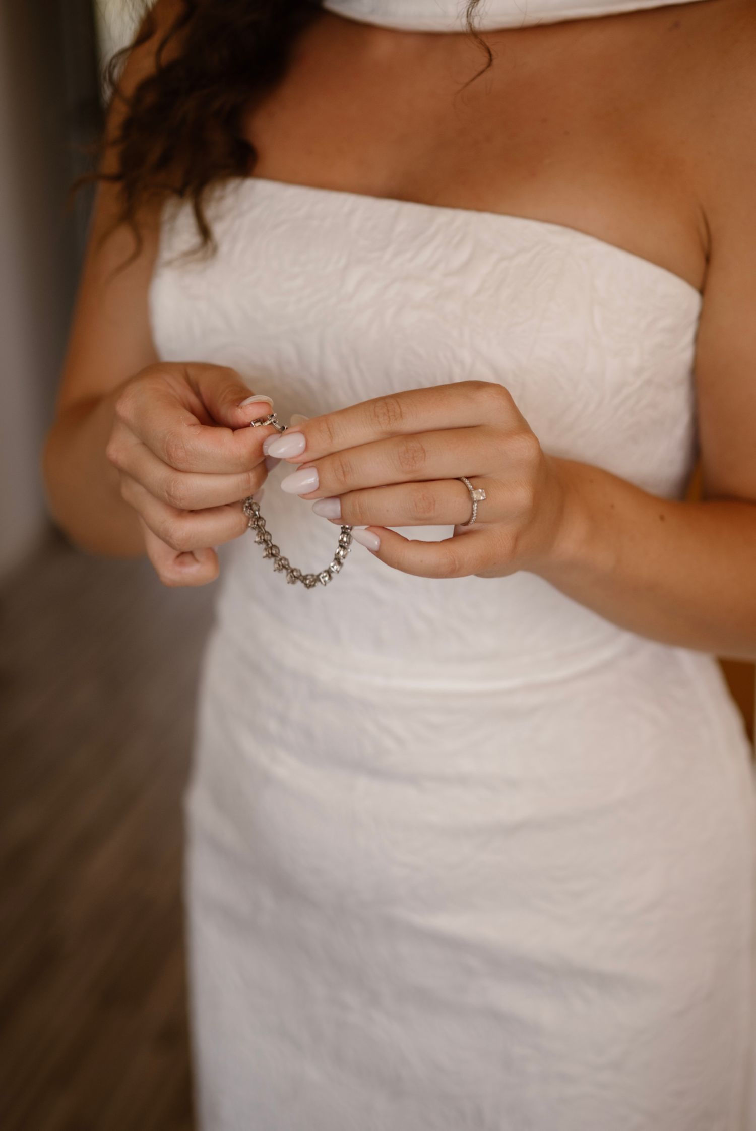 Bride in white strapless wedding dress holding a diamond bracelet with manicured nails and engagement ring.