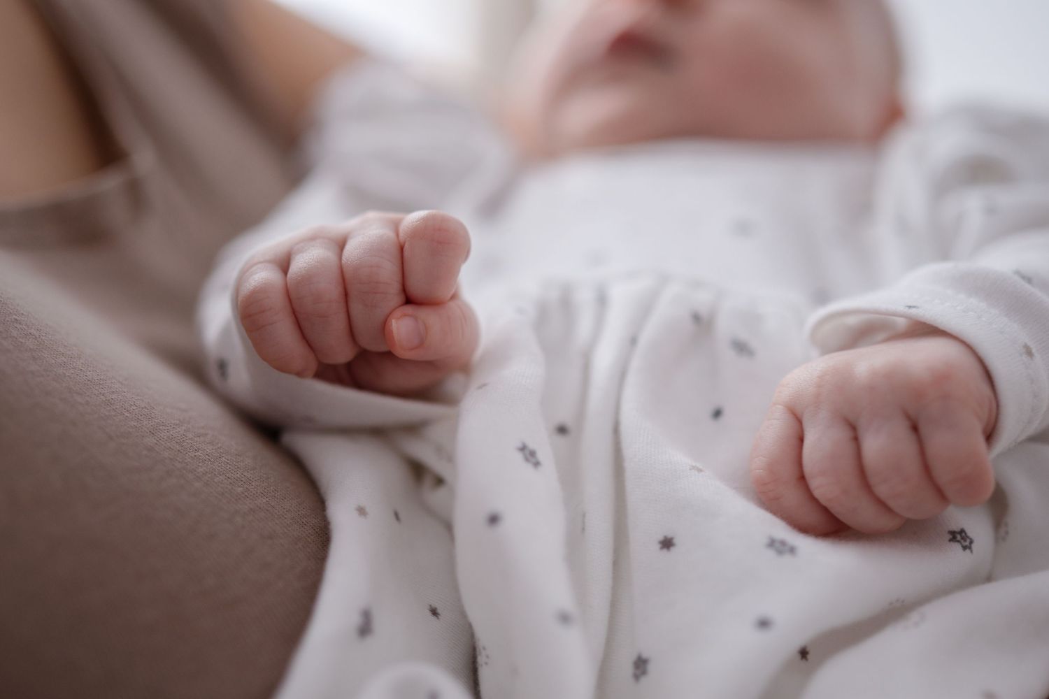 A close-up view of tiny newborn baby hands grasping and reaching against a soft white fabric background.