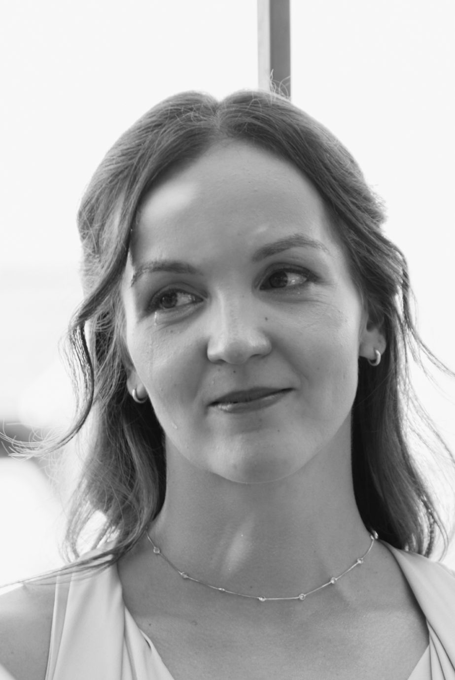 Elegant bride in white dress wearing a delicate necklace and earrings, black and white portrait photo.