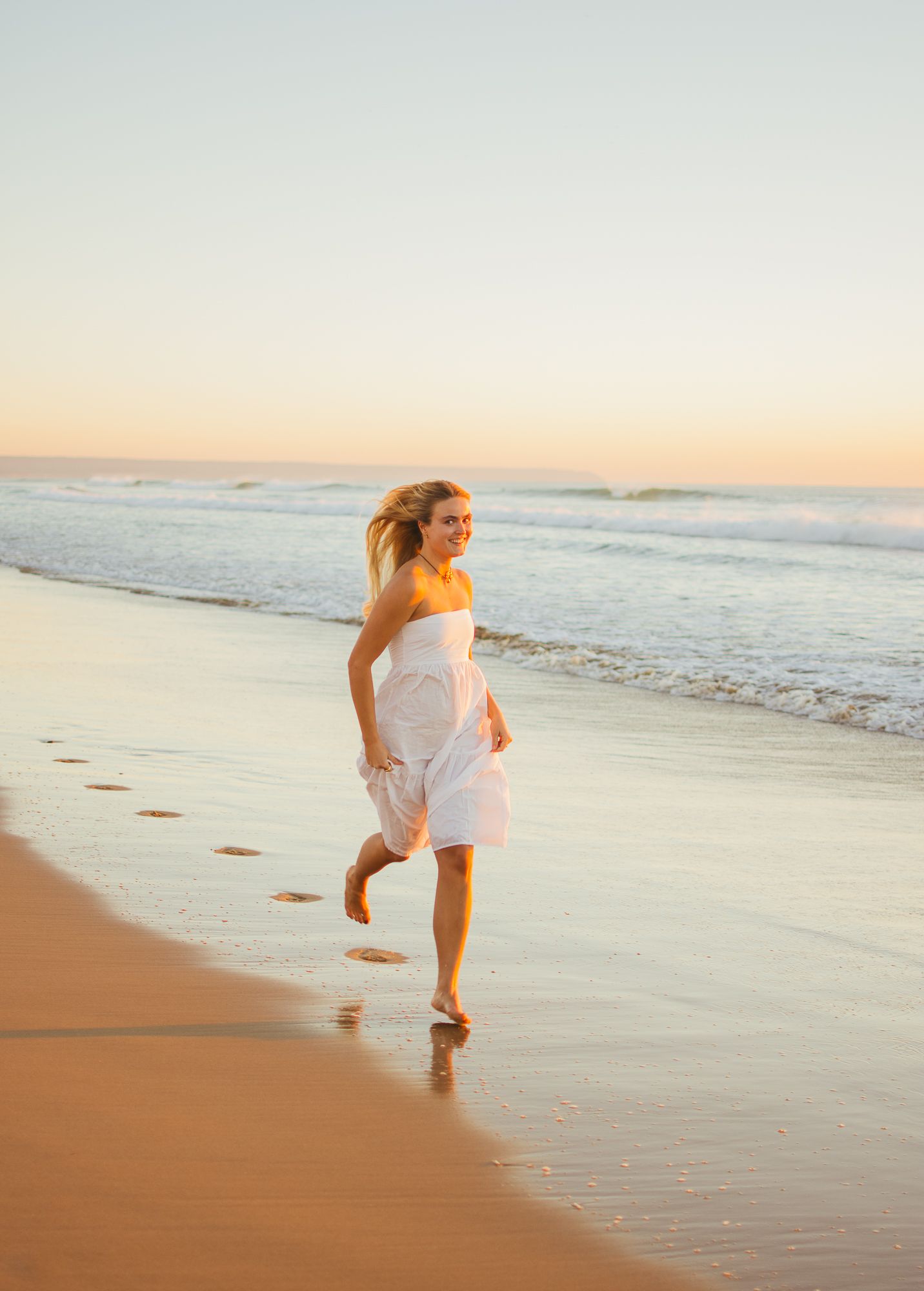 Playful couple running and splashing along a sunset beach in white clothing.