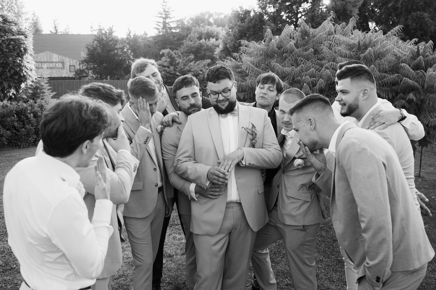 Wedding party members in light gray suits share candid moments during outdoor photo session.