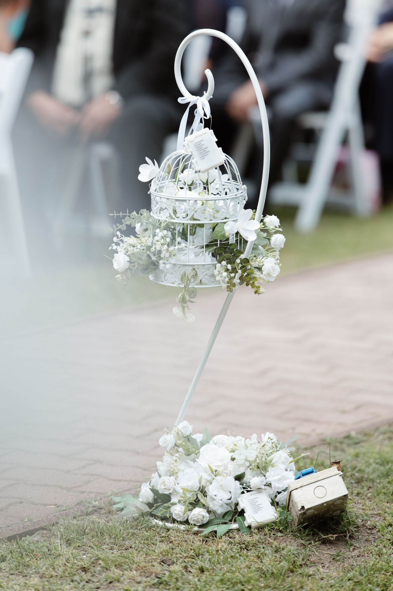 White floral decorations hanging on shepherd's hooks along an outdoor pathway.