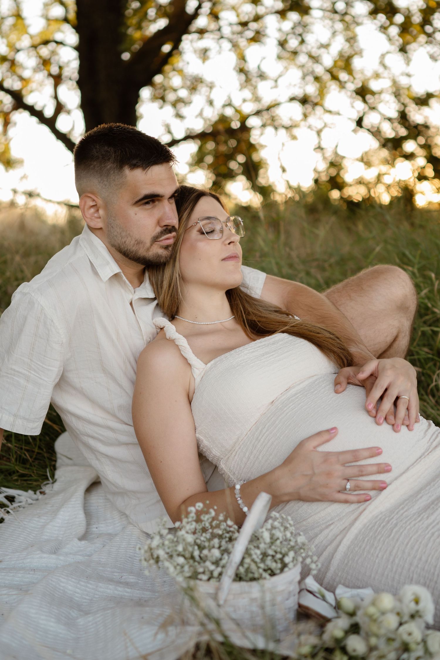 Romantic maternity photoshoot in a field with white baby's breath flowers at sunset.