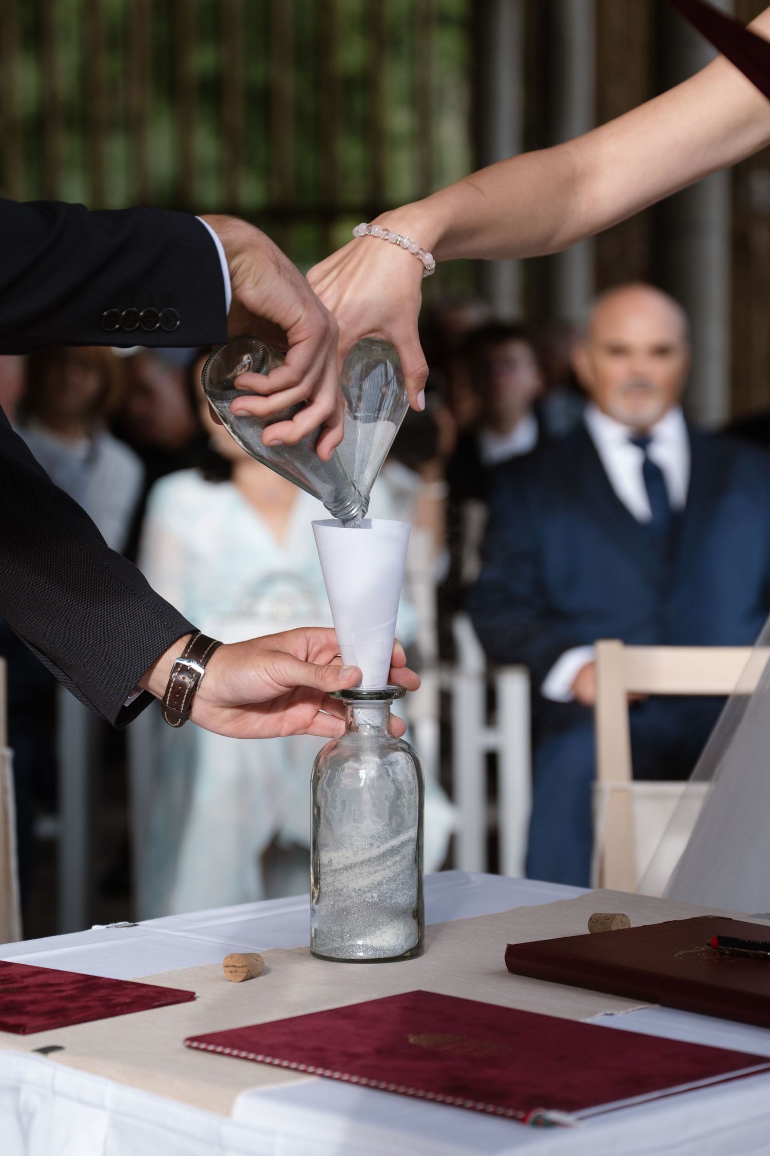 Wedding guests participate in a sand pouring unity ceremony ritual during an outdoor celebration.