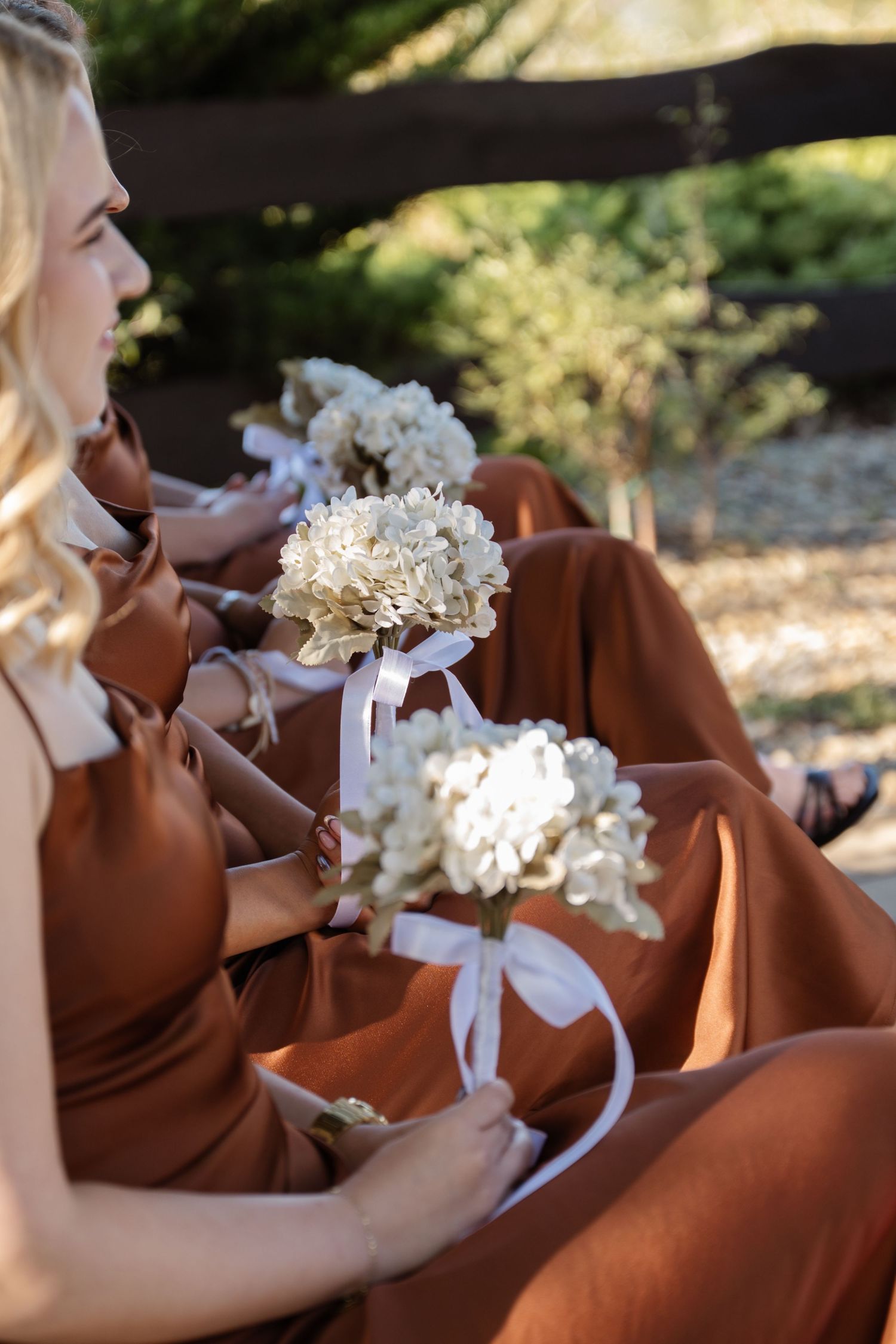 Row of bridesmaids in brown dresses holding white floral bouquets.