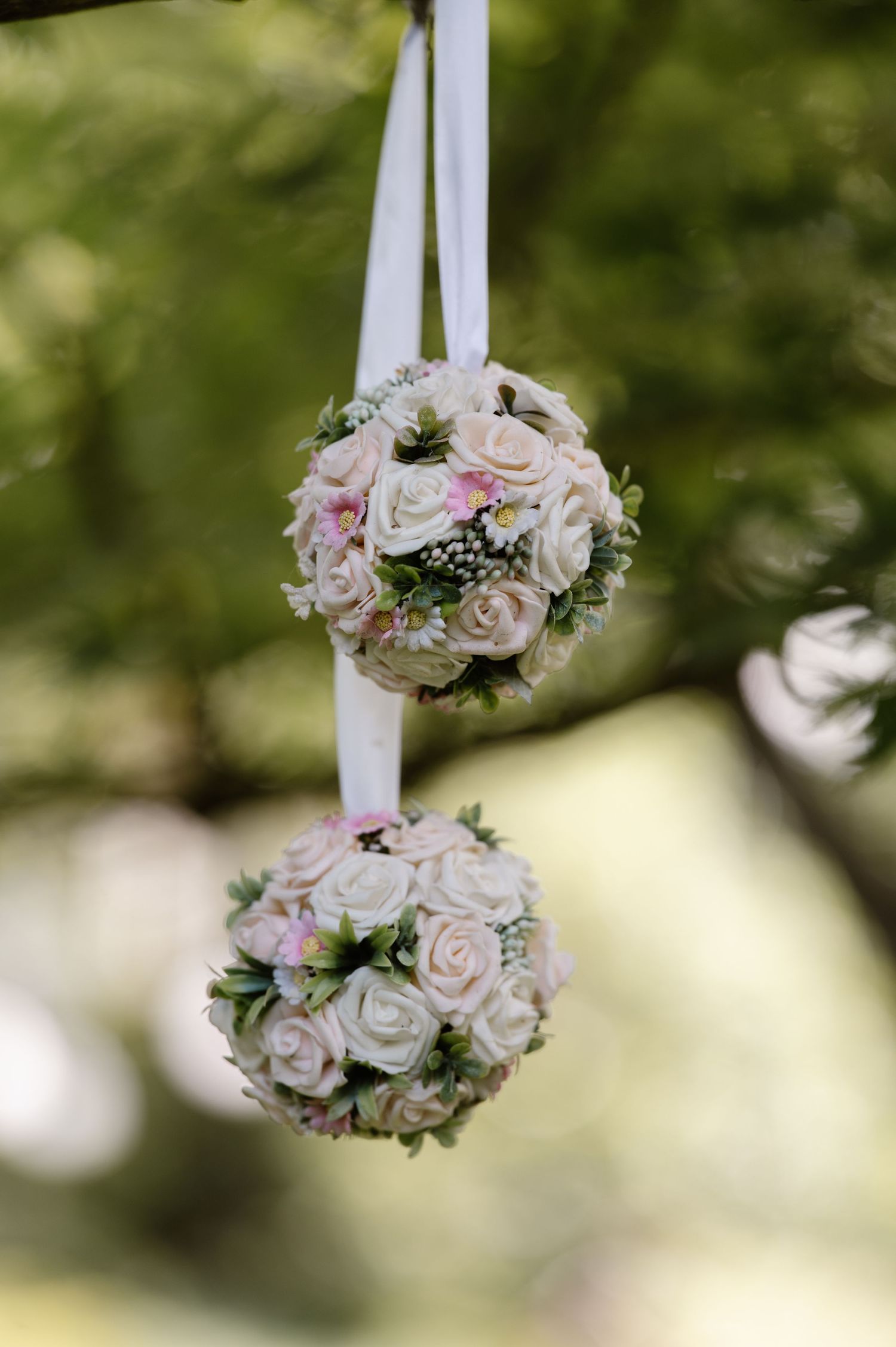Delicate pink and white rose pomanders hanging from ribbons for wedding decoration.