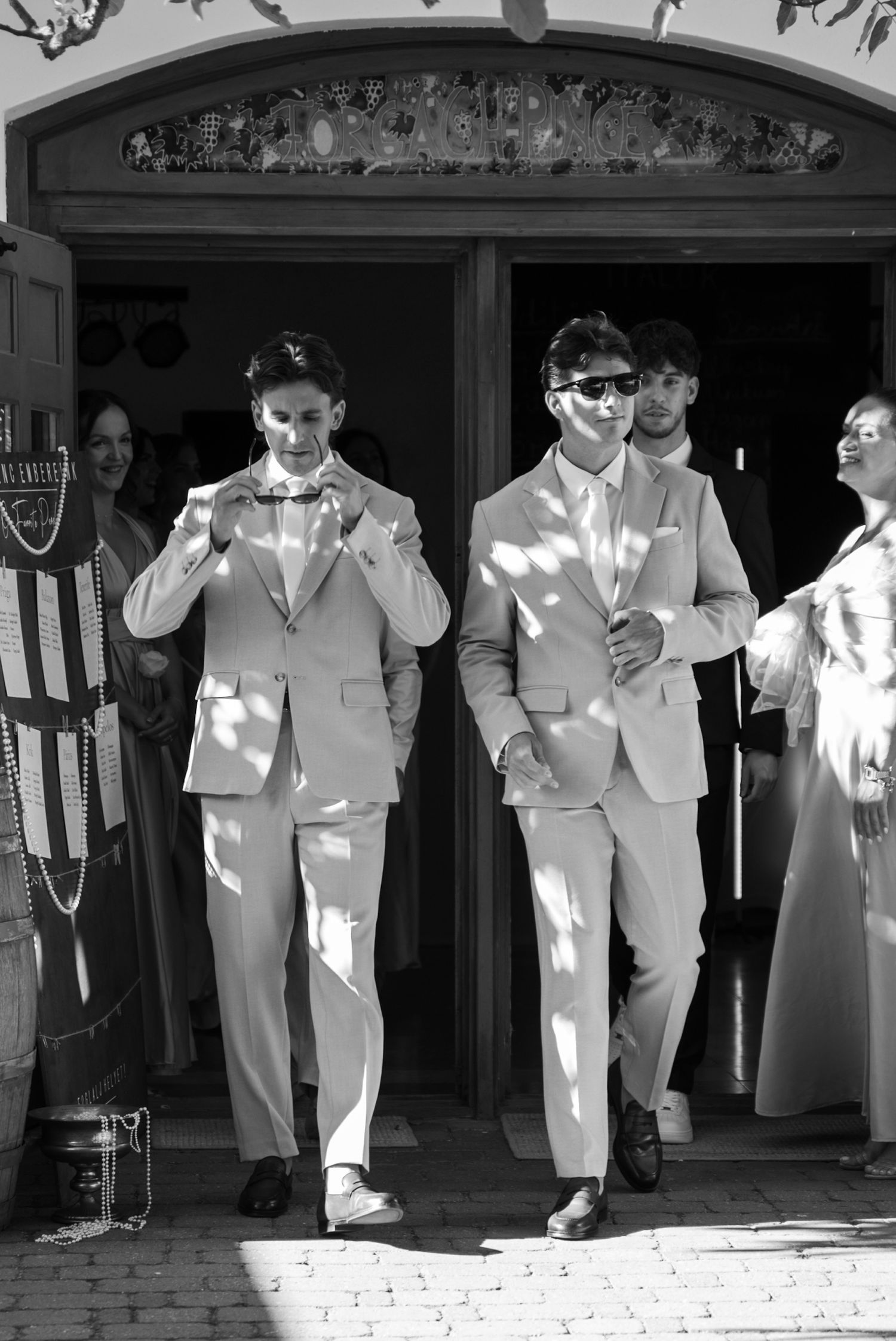 Two groomsmen in matching light gray suits exiting church doors in black and white wedding photography.