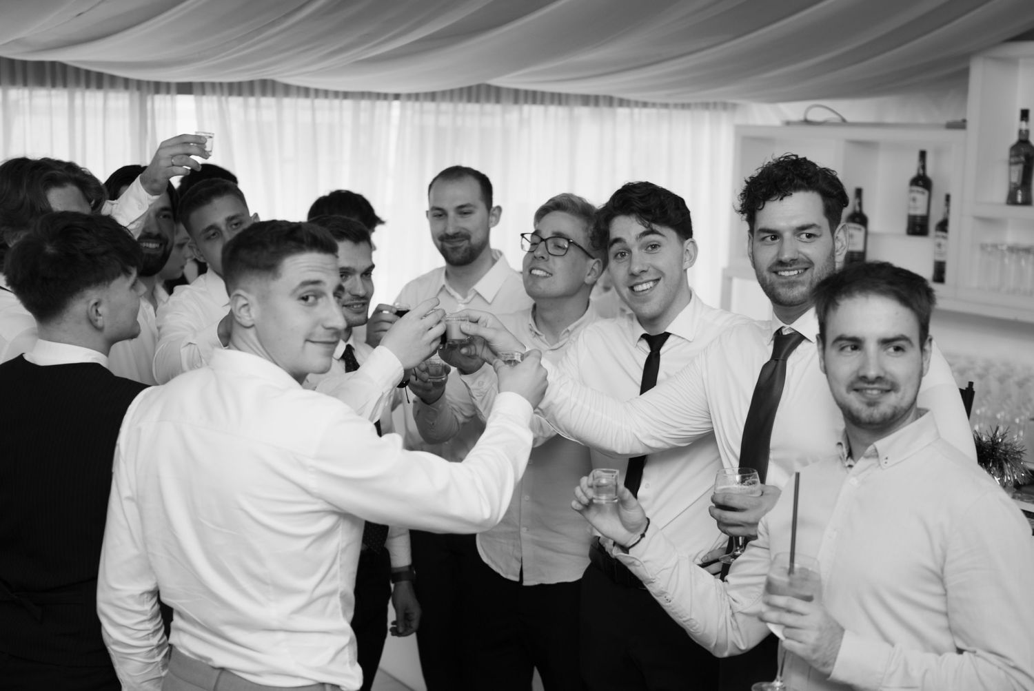 Group of men in white shirts celebrating together at a formal indoor event in black and white photo.