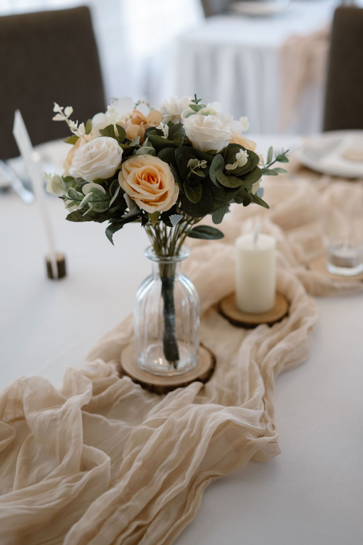Elegant wedding table decor with peach roses, candles and flowing fabric runner.