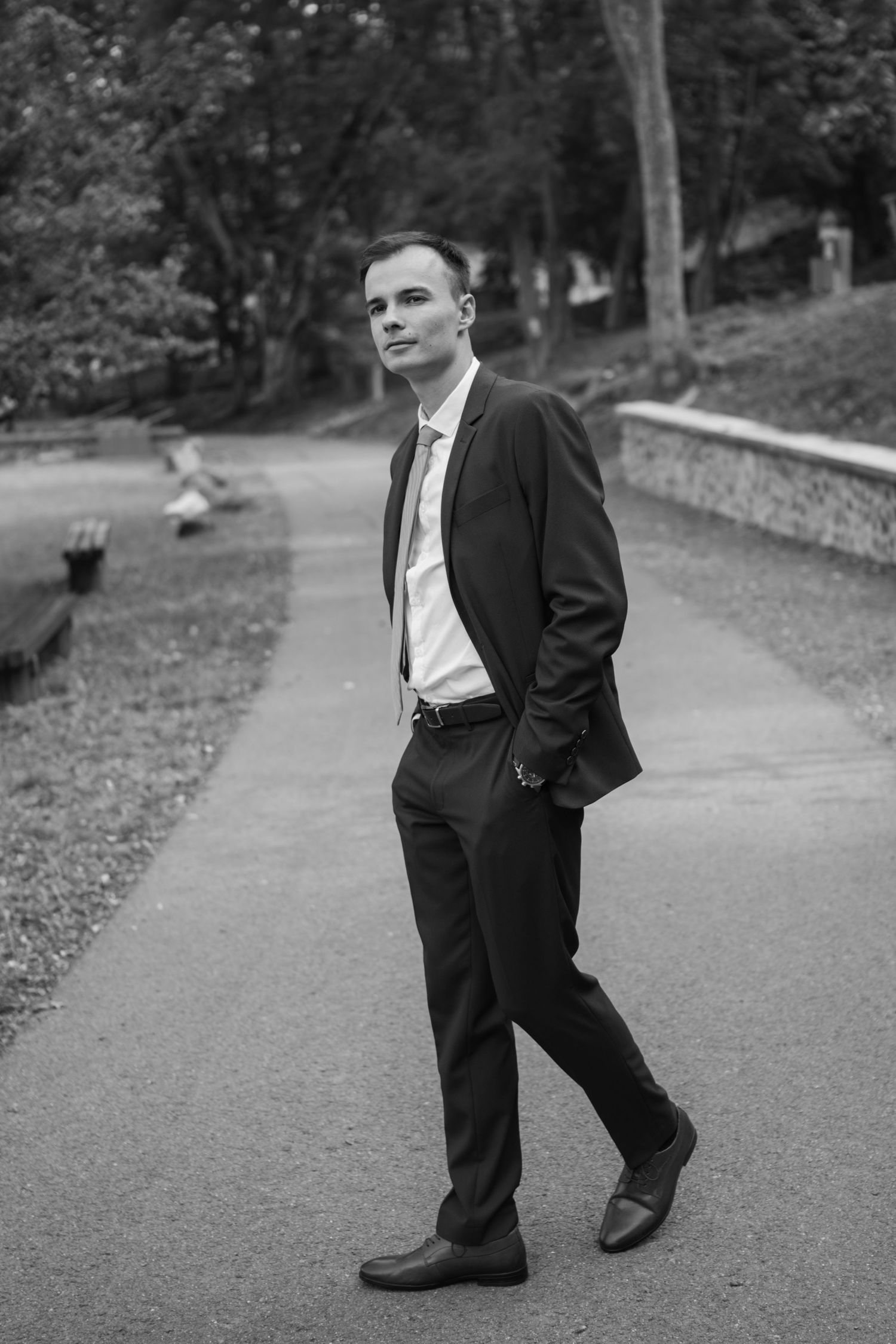 Black and white portrait of a groom in formal attire on a garden path.