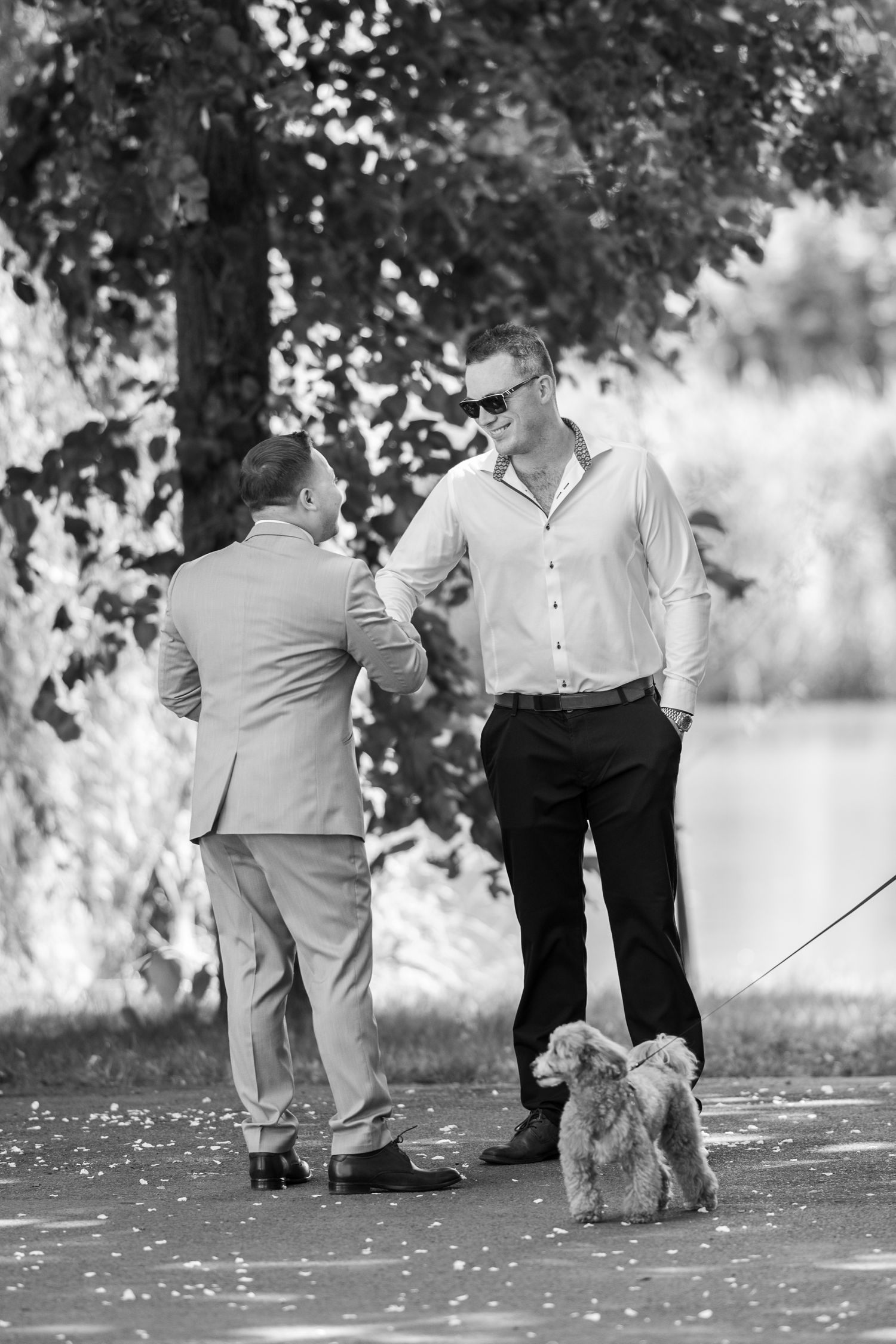 Two men having a conversation outdoors with a small dog at their feet.